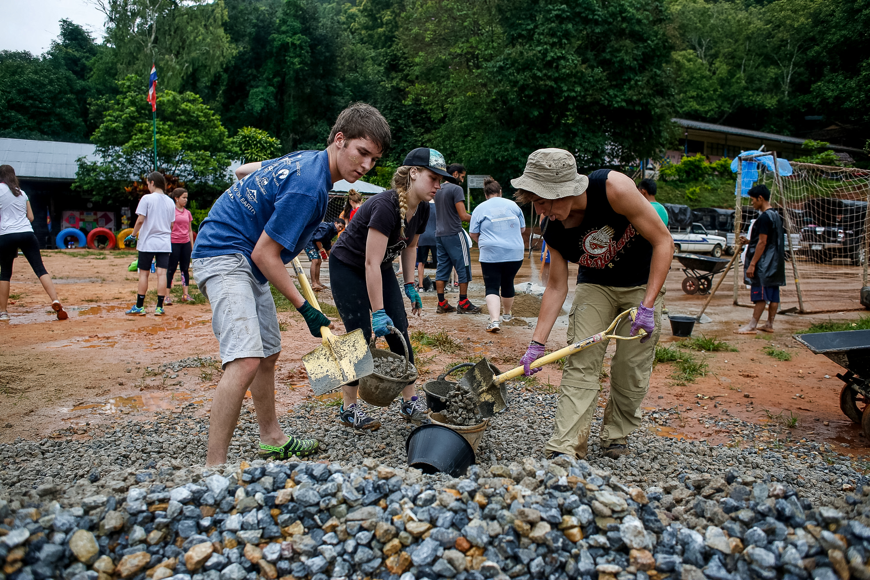 Students shovel gravel and cement into buckets at an outdoor worksite