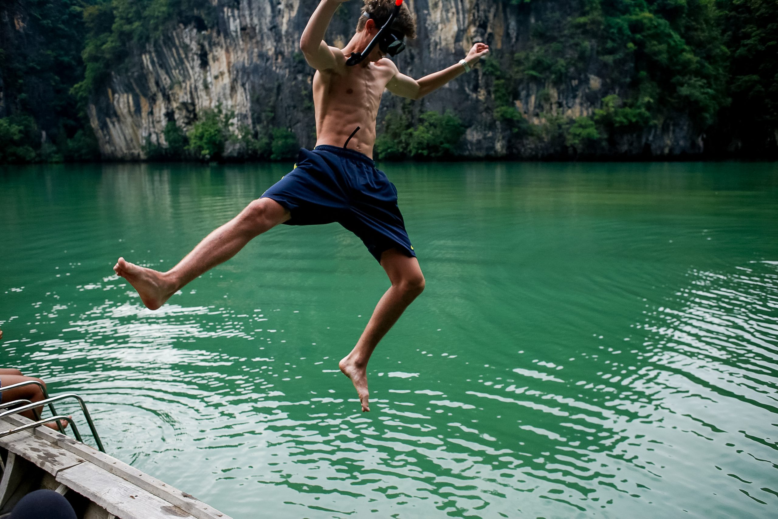 A student leaps off a boat into green water surrounded by limestone cliffs