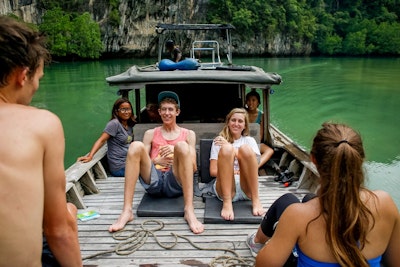 students sitting on a wooden boat enjoying the natural scenery during a teen travel program in Thailand