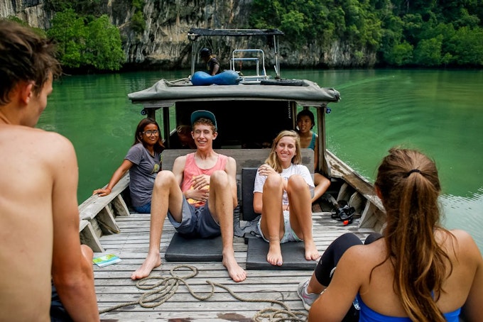 Students sitting on a wooden boat enjoying the natural scenery during a travel program in Thailand