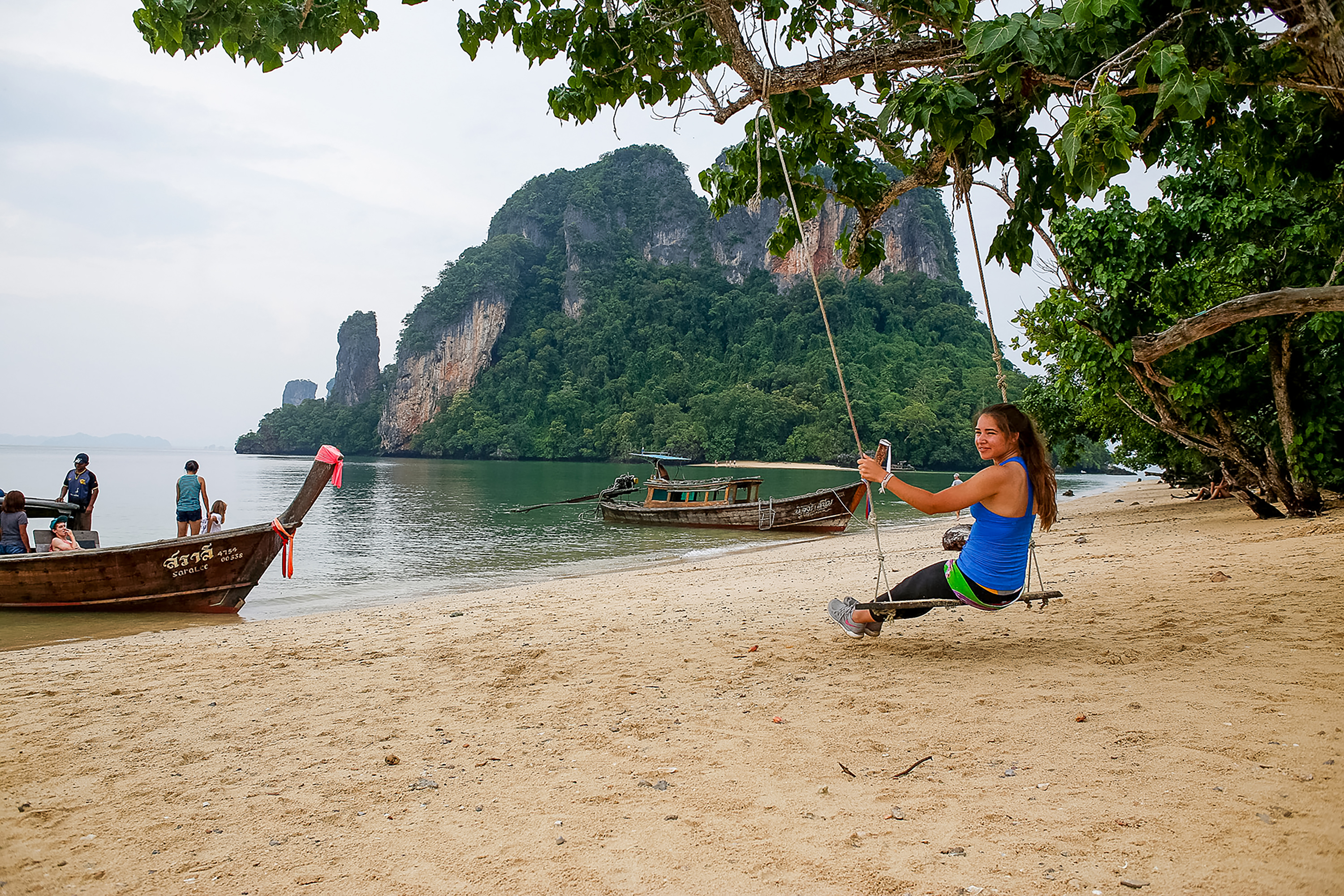 Girl on a swing in the beach in Thailand with other students getting on a boat.