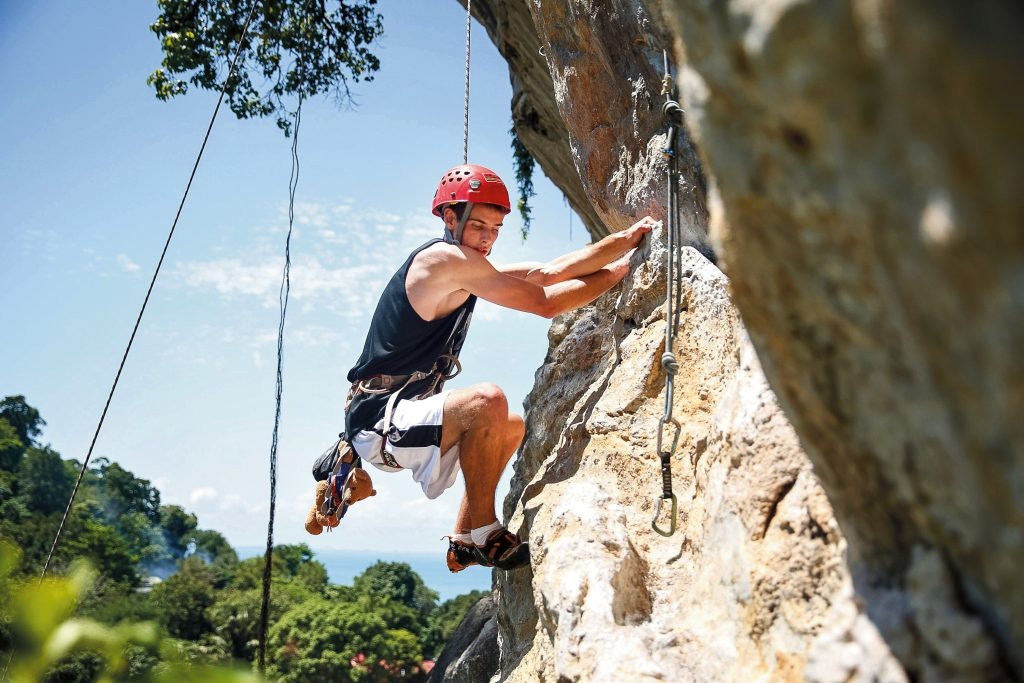 Teen rock climbing on limestone cliffs in Krabi, Thailand with the sea in the background.