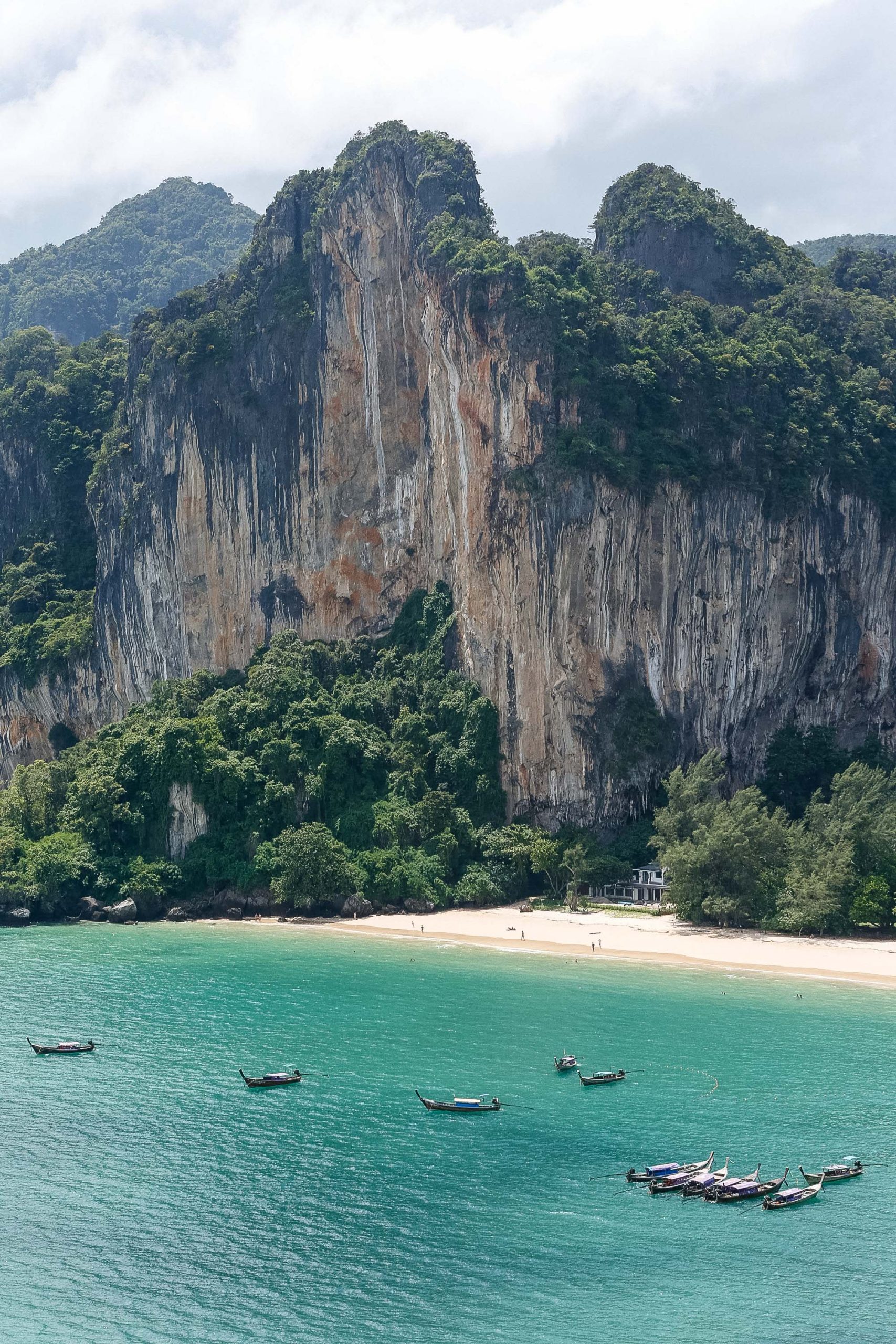 Longtail boats float in turquoise water beneath towering limestone cliffs