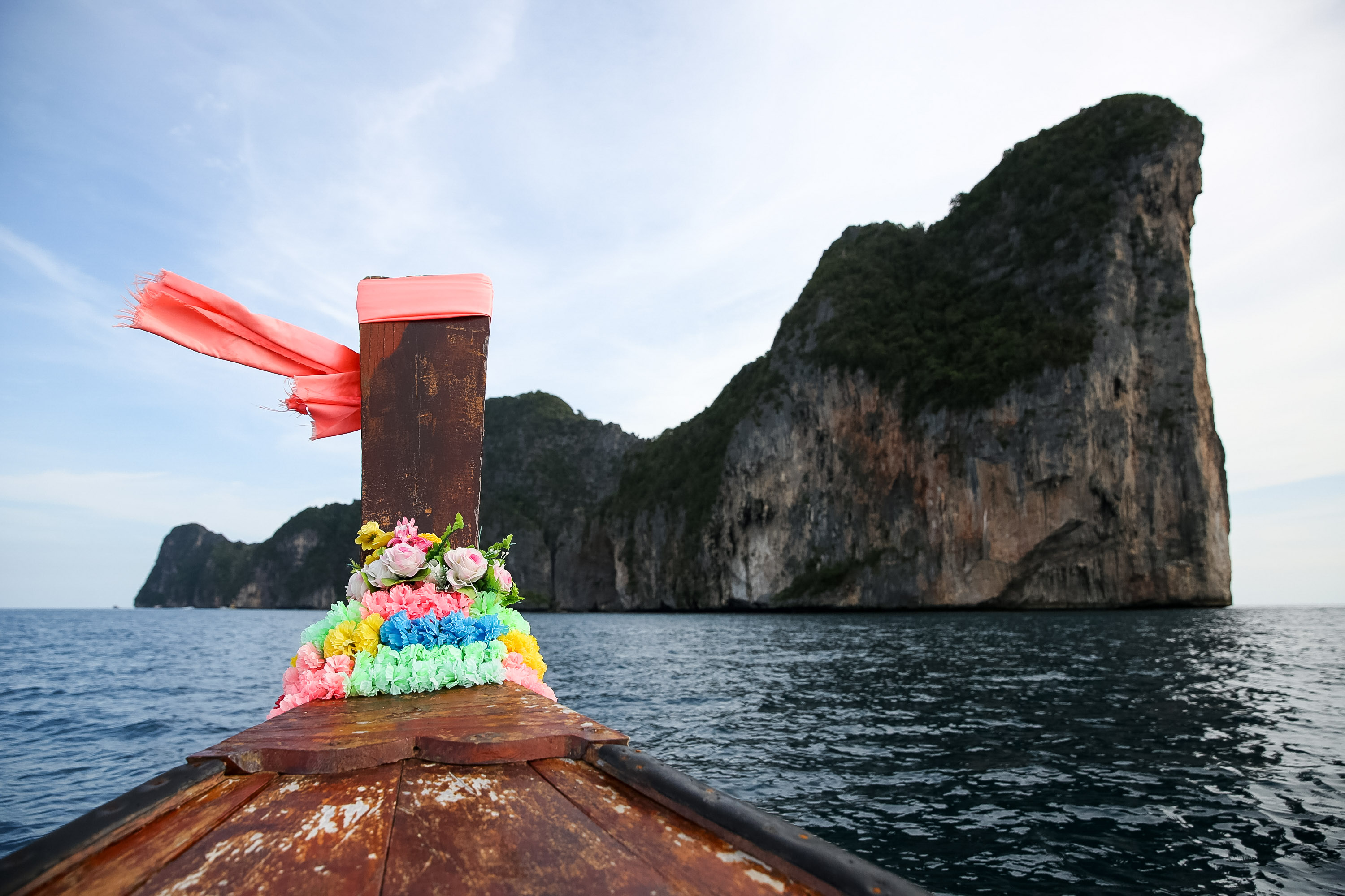 A traditional longtail boat in Thailand rests with its flower-decorated bow facing a limestone island cliff