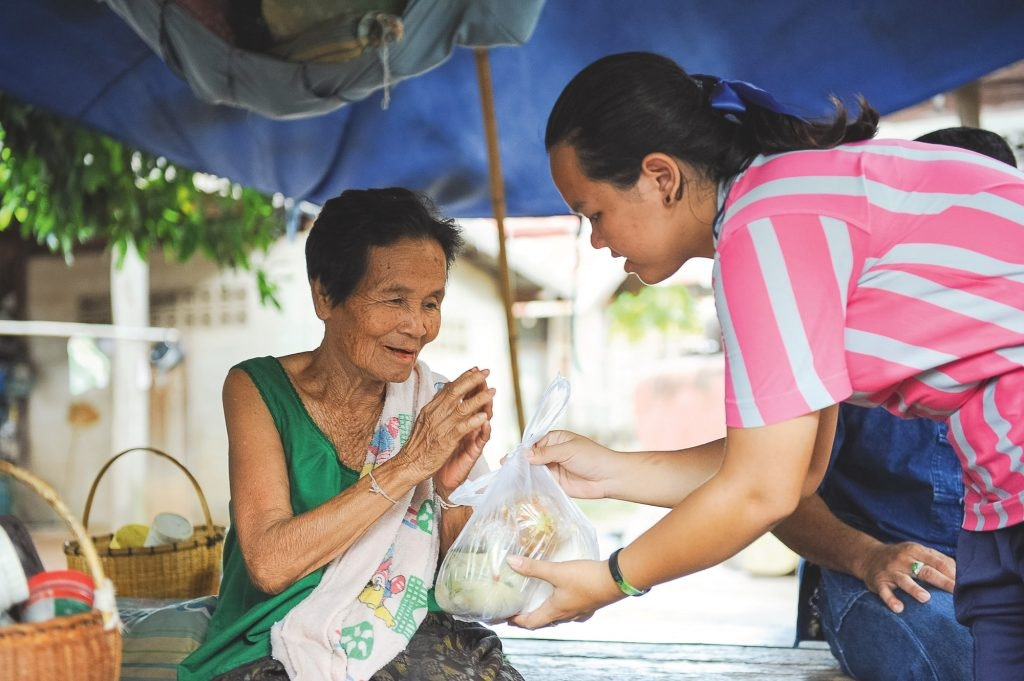 A volunteer shares food and compassion with an elderly woman in Thailand, showing the spirit of public health volunteering abroad through community care and connection.