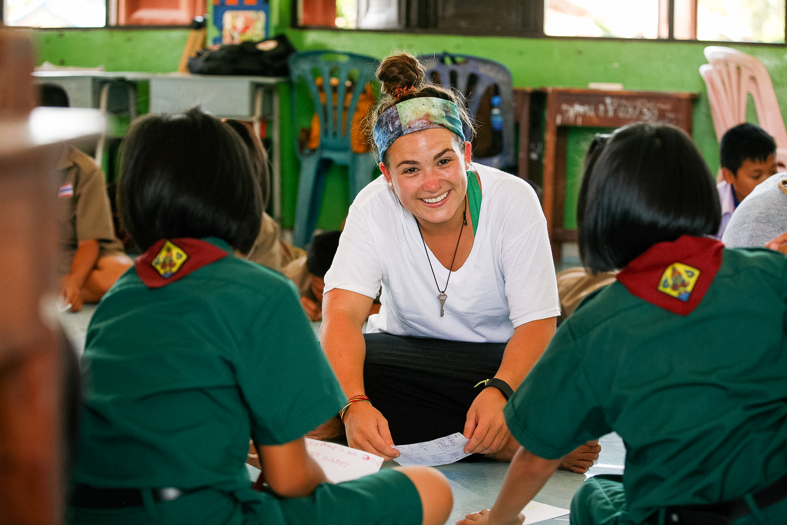 A leader smiles while sitting on the floor with students in uniform during a classroom activity