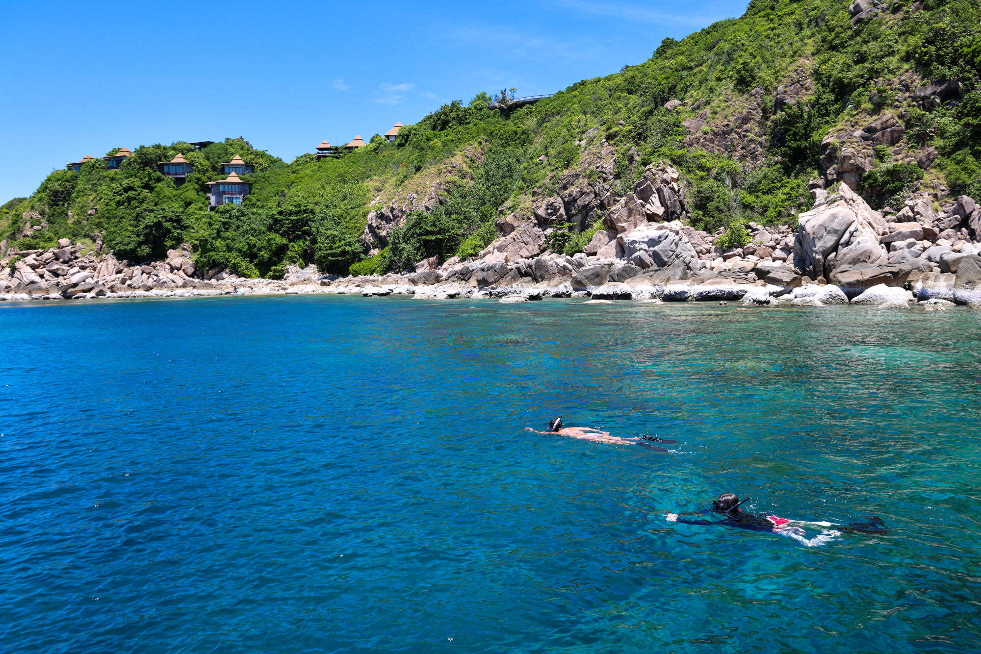Snorkelers swim along a rocky, forested coastline in Thailand