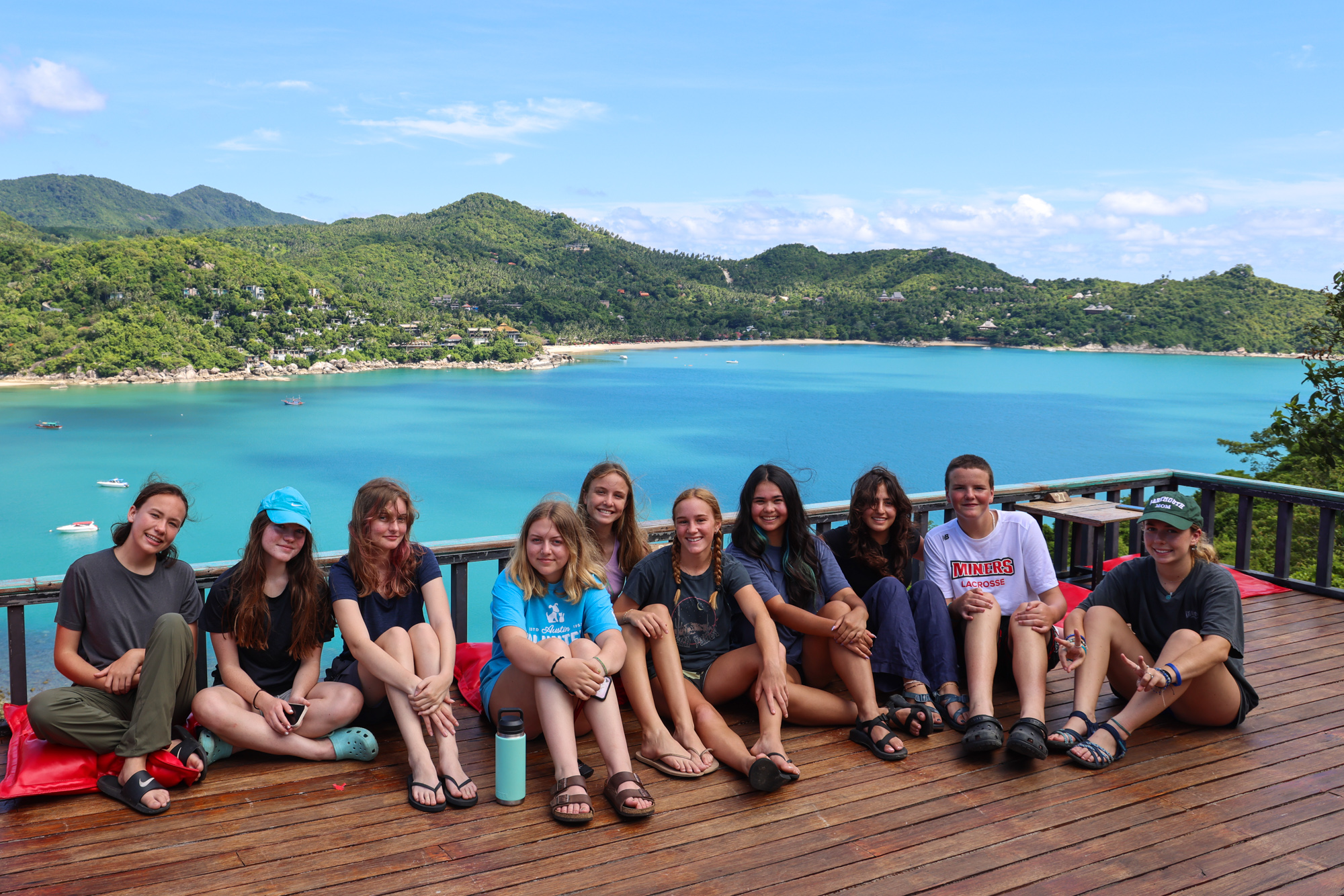 Students sitting down together with view of ocean and mountains in the background in Thailand.