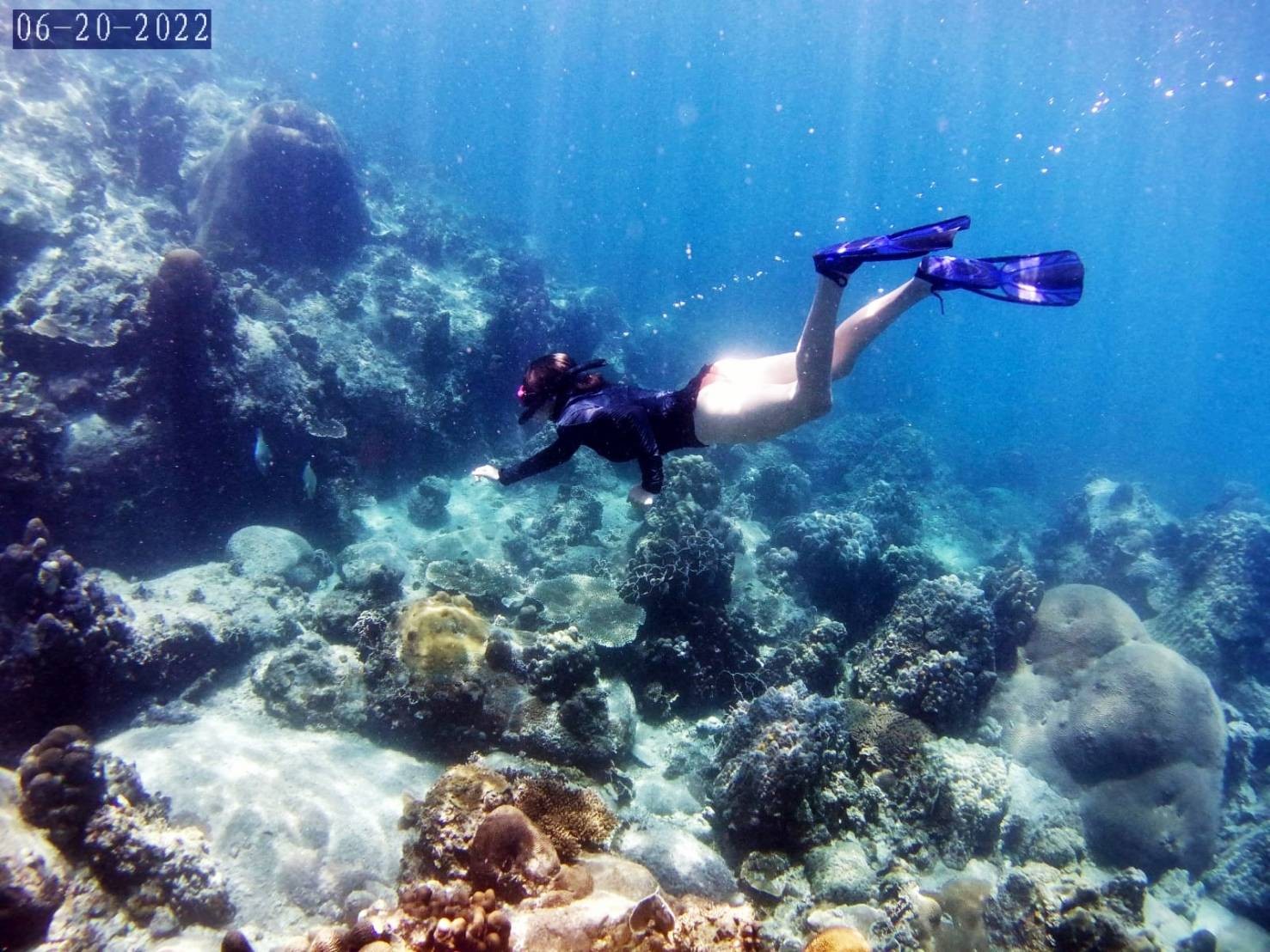 A snorkeler with fins glides over a coral reef in the Andaman Sea
