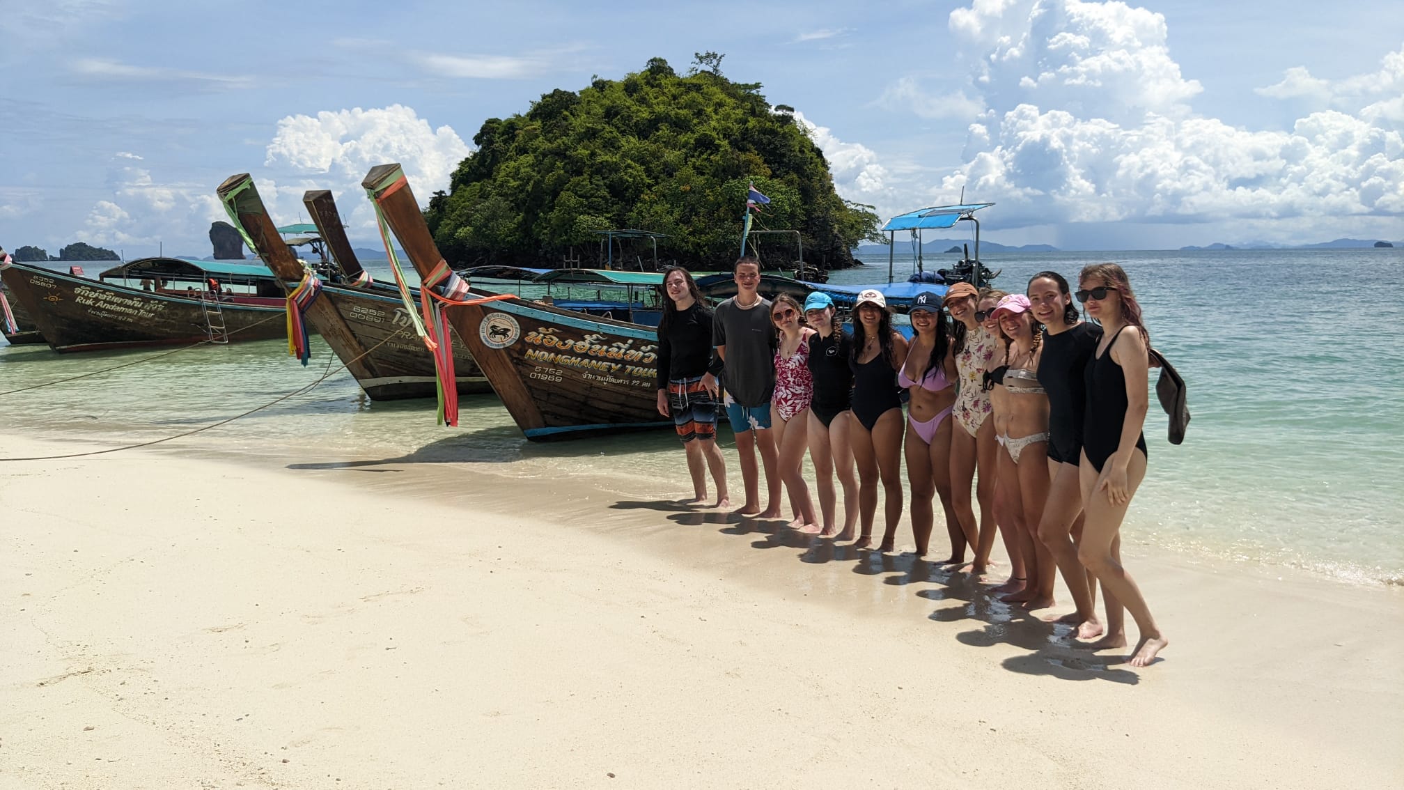 Group of students posing in the beach in Thailand next to boats.