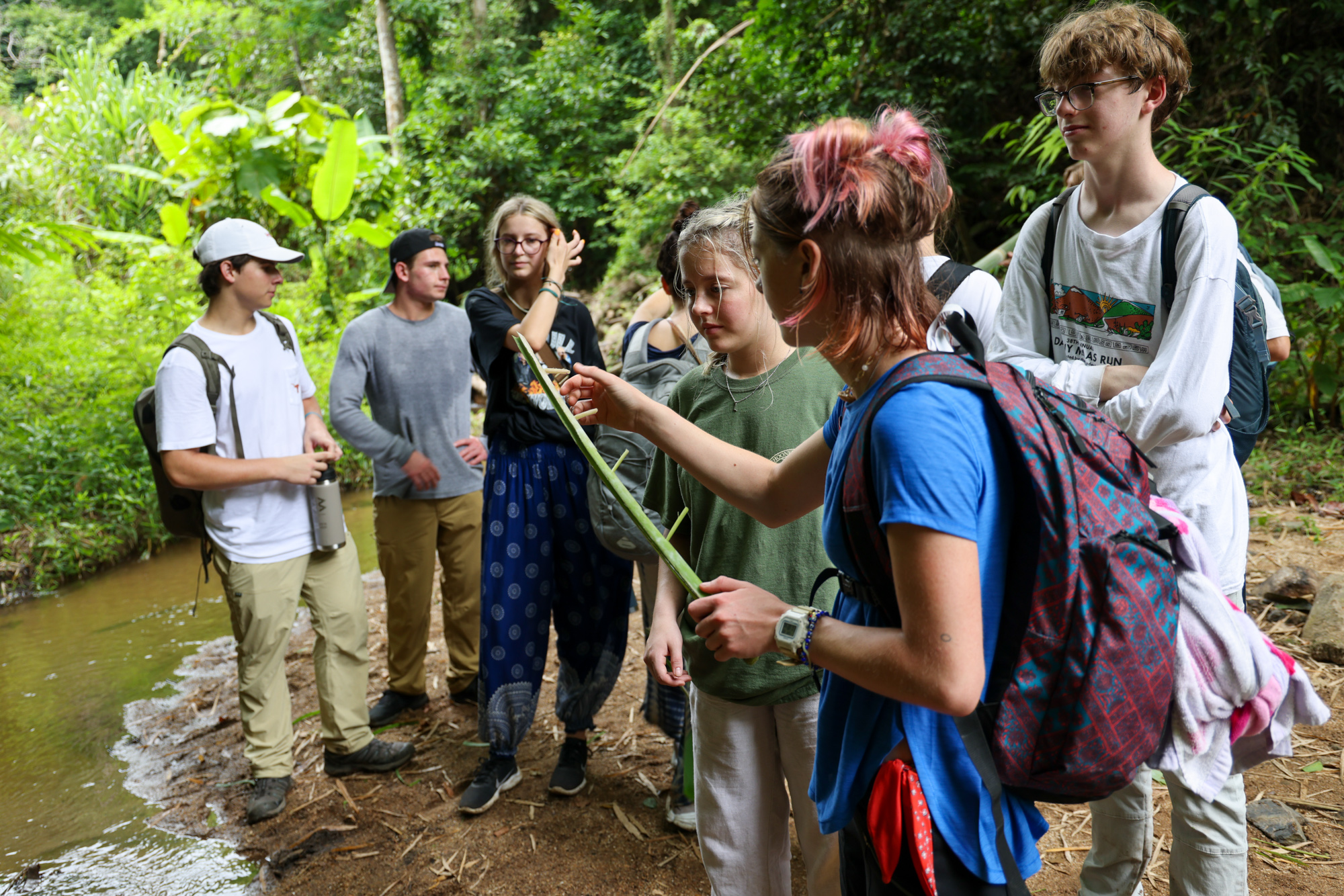 Students gathered together near puddle of water and trees in the background in Thailand.