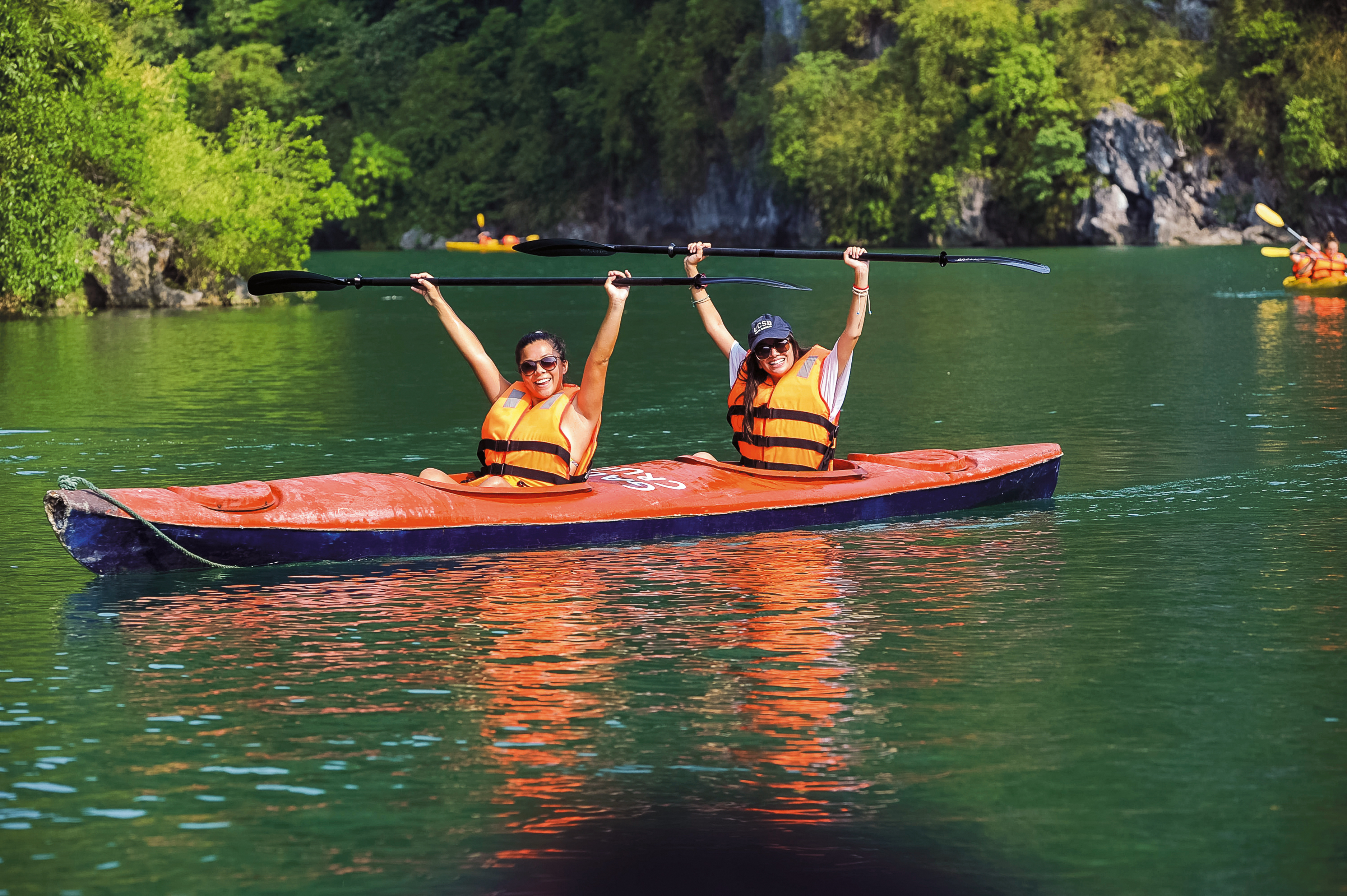 Students raise their paddles while kayaking on Halong Bay's green water