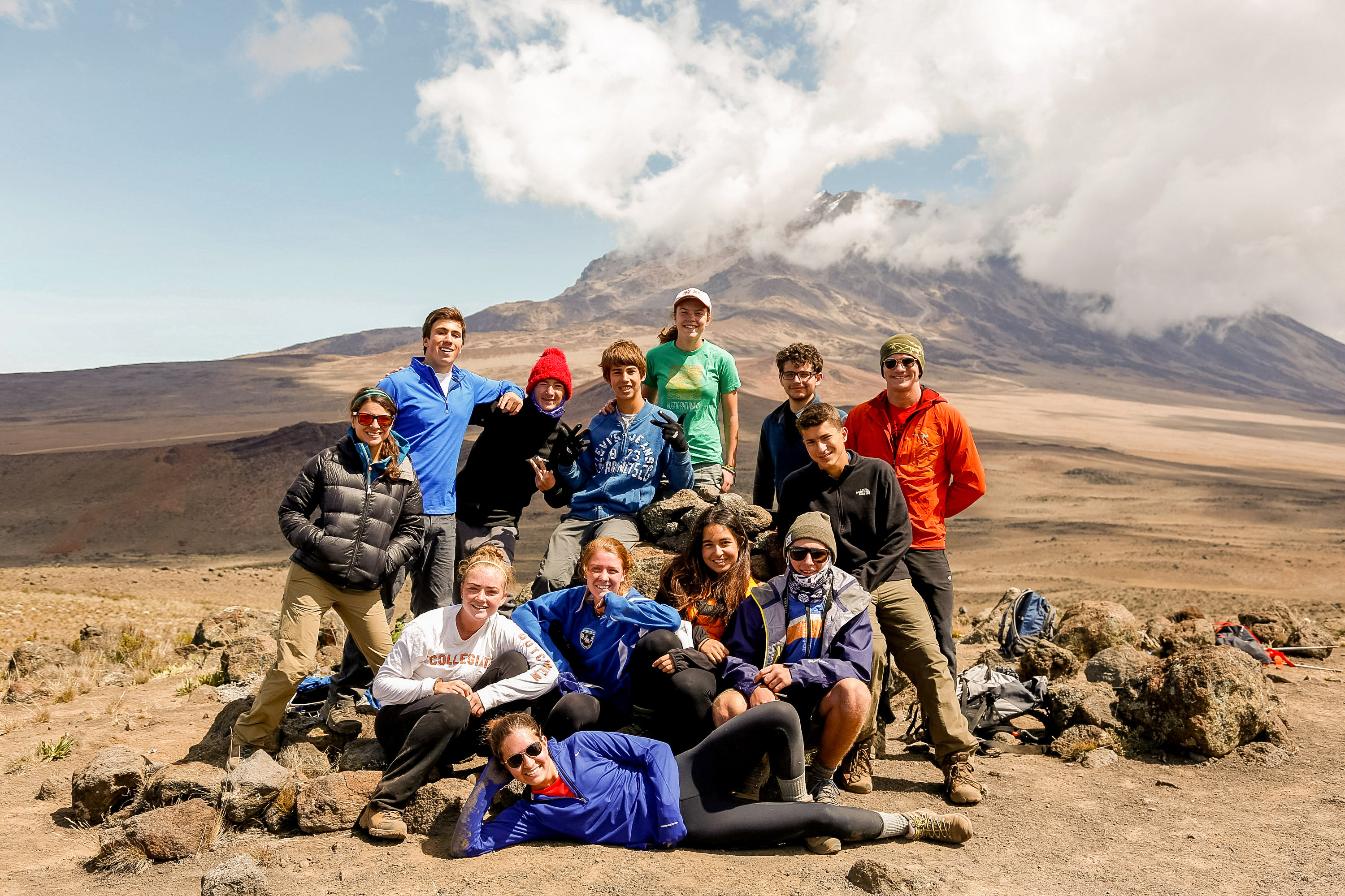 Students pose together on a rocky slope with a cloud-wrapped peak behind them