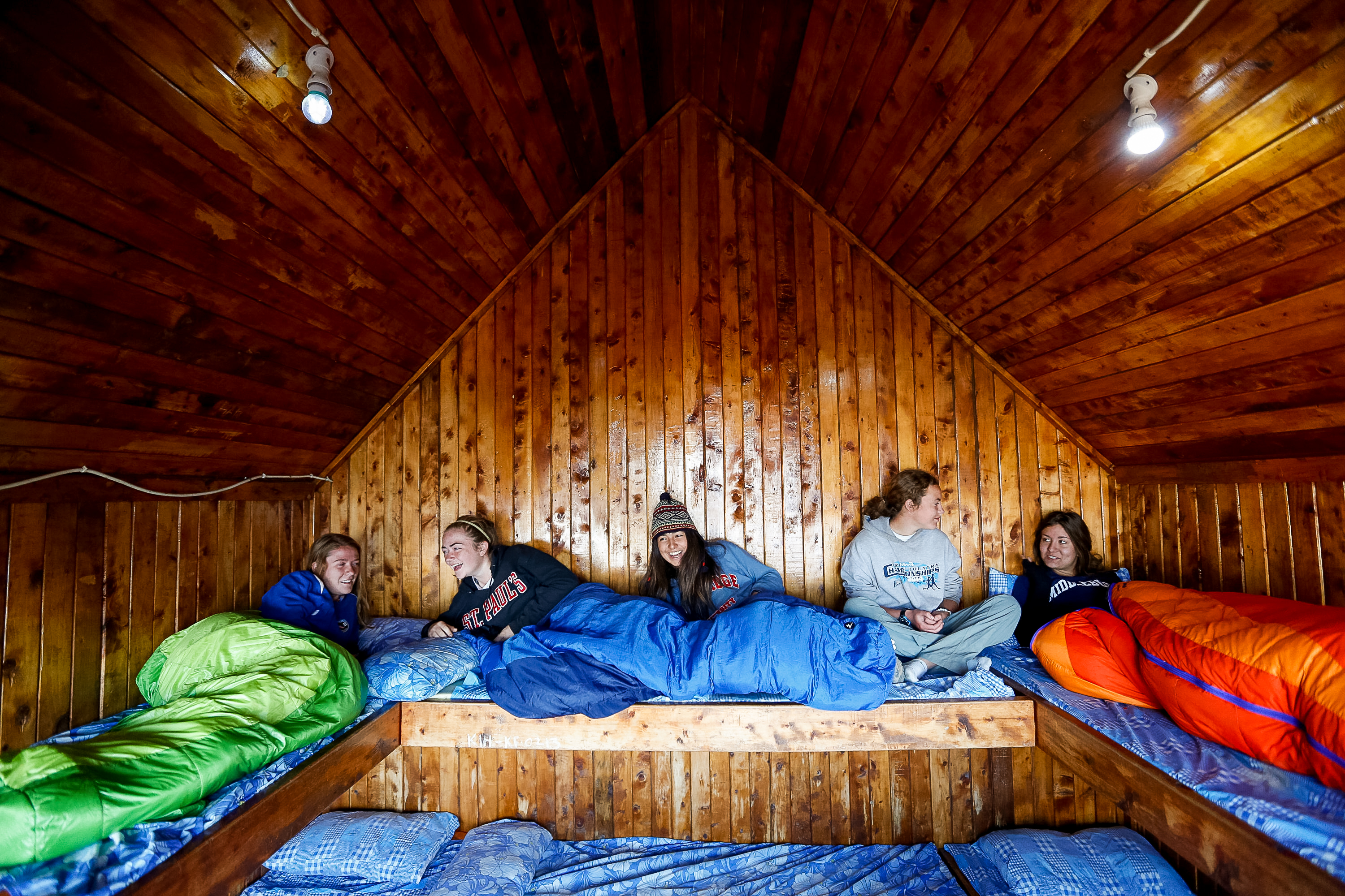 Students rest in sleeping bags along a wooden mountain hut sleeping platform