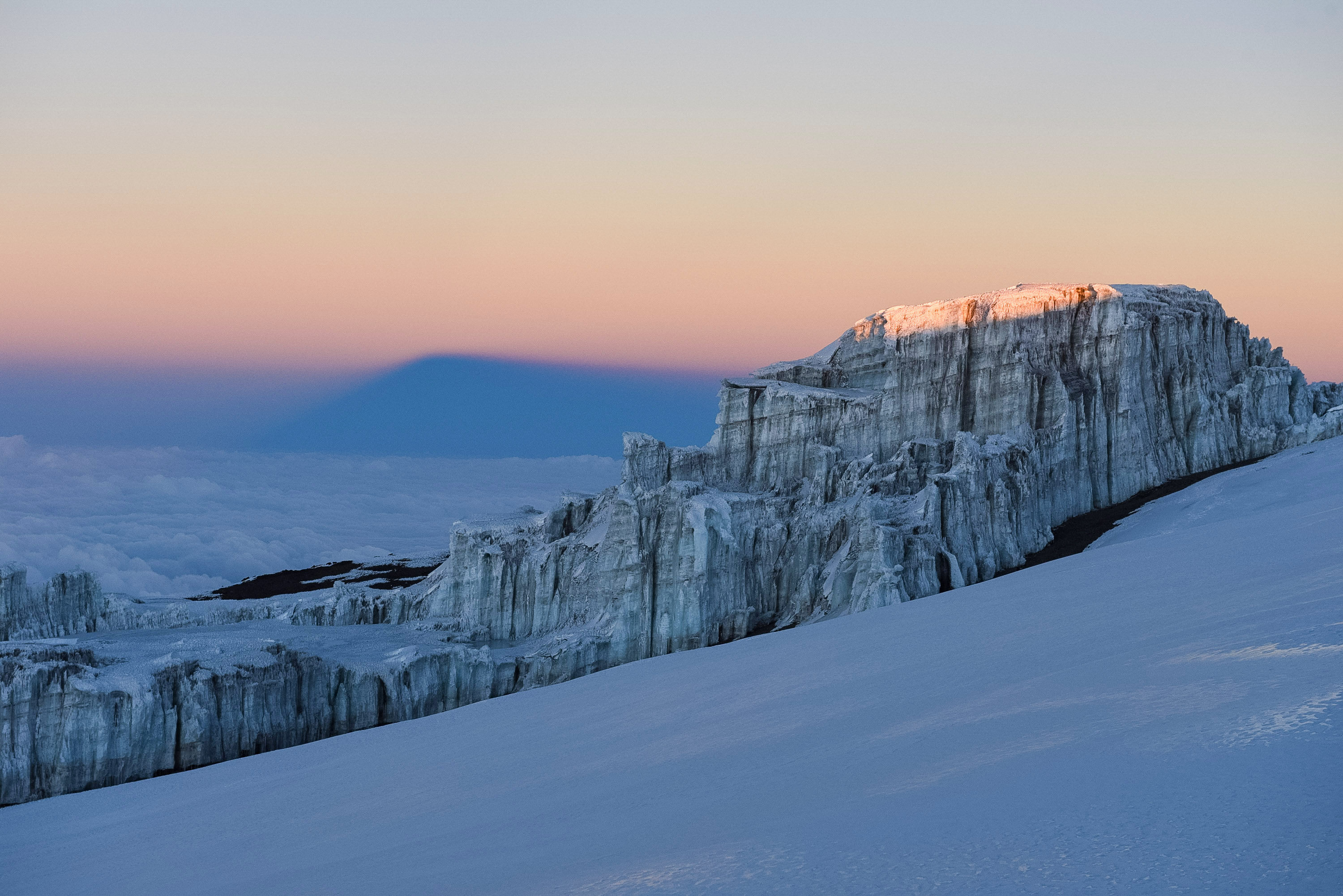 Glacial ice cliffs near Kilimanjaro's summit glow at sunrise with a shadow cast across the sky