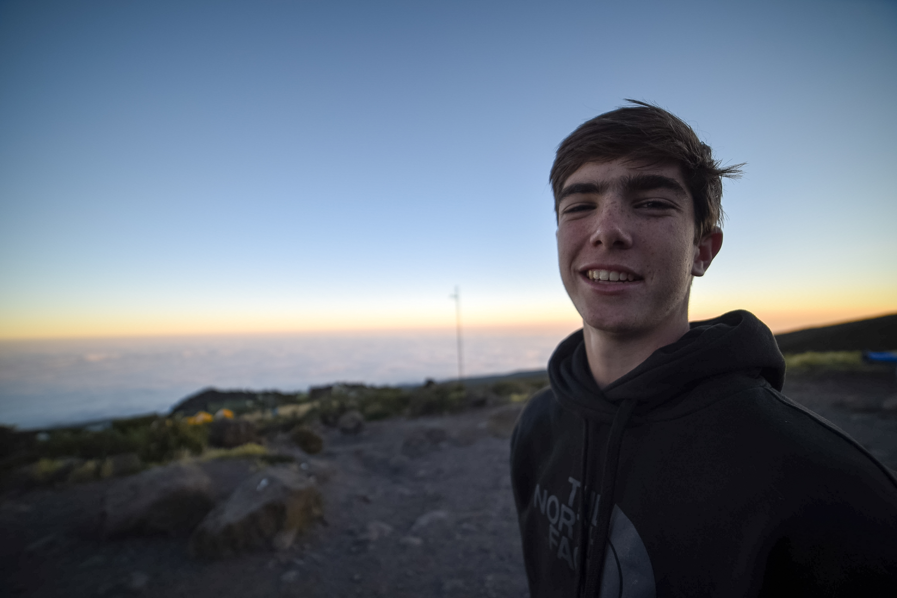 A student smiles at sunrise above a sea of clouds on Kilimanjaro
