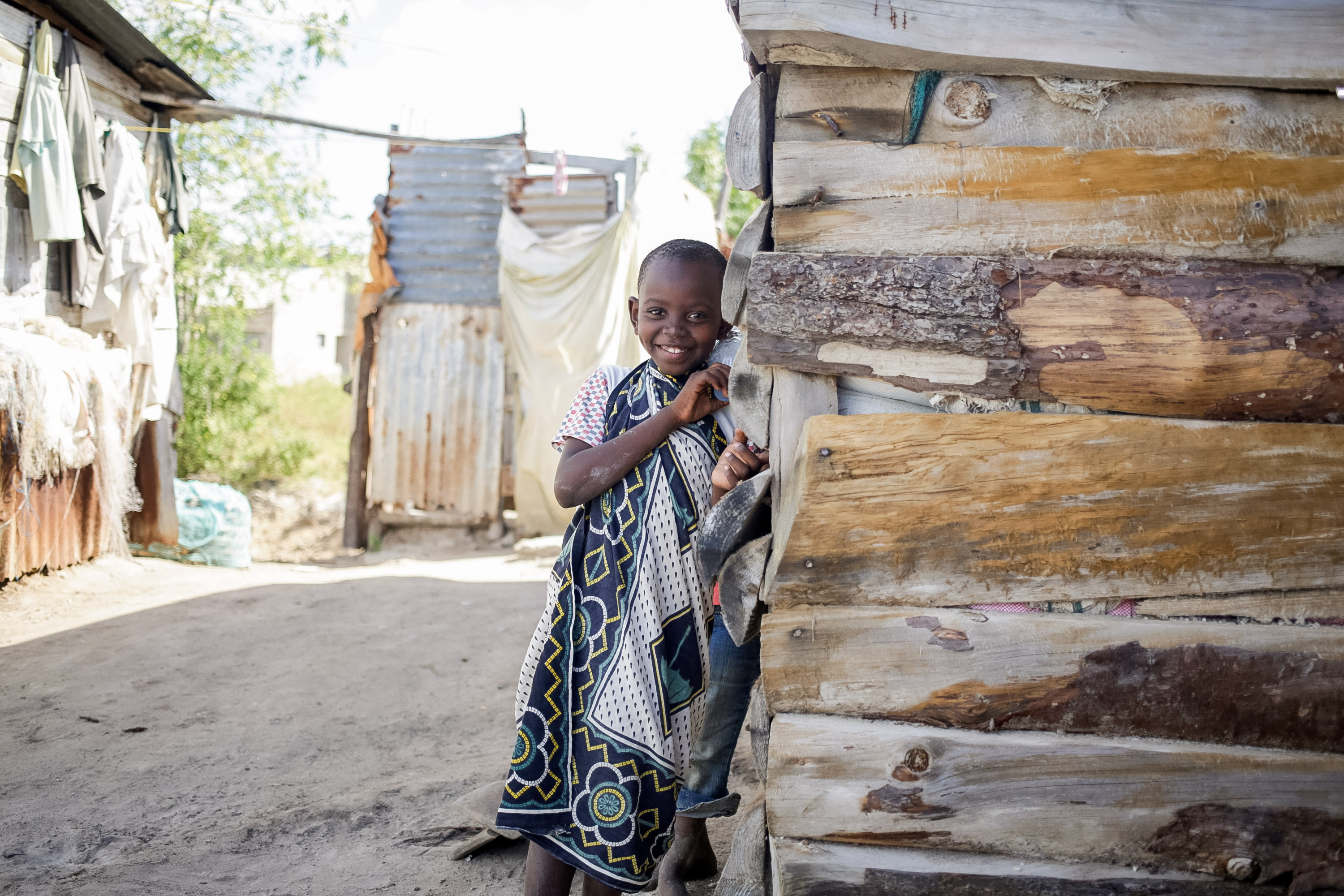Student travelers pause beside a wooden shack while a child smiles in a coastal village