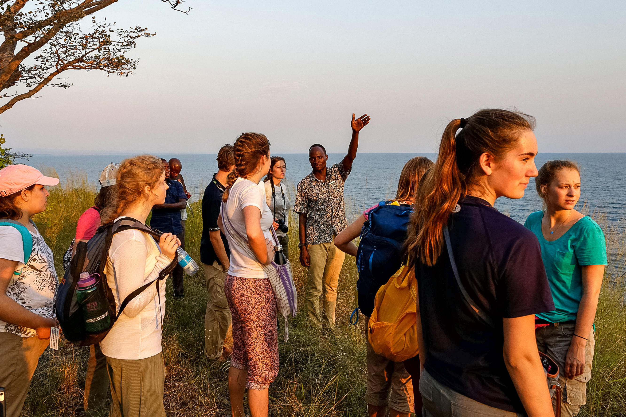 Students gather on a coastal hillside as a guide gestures toward the ocean at dusk