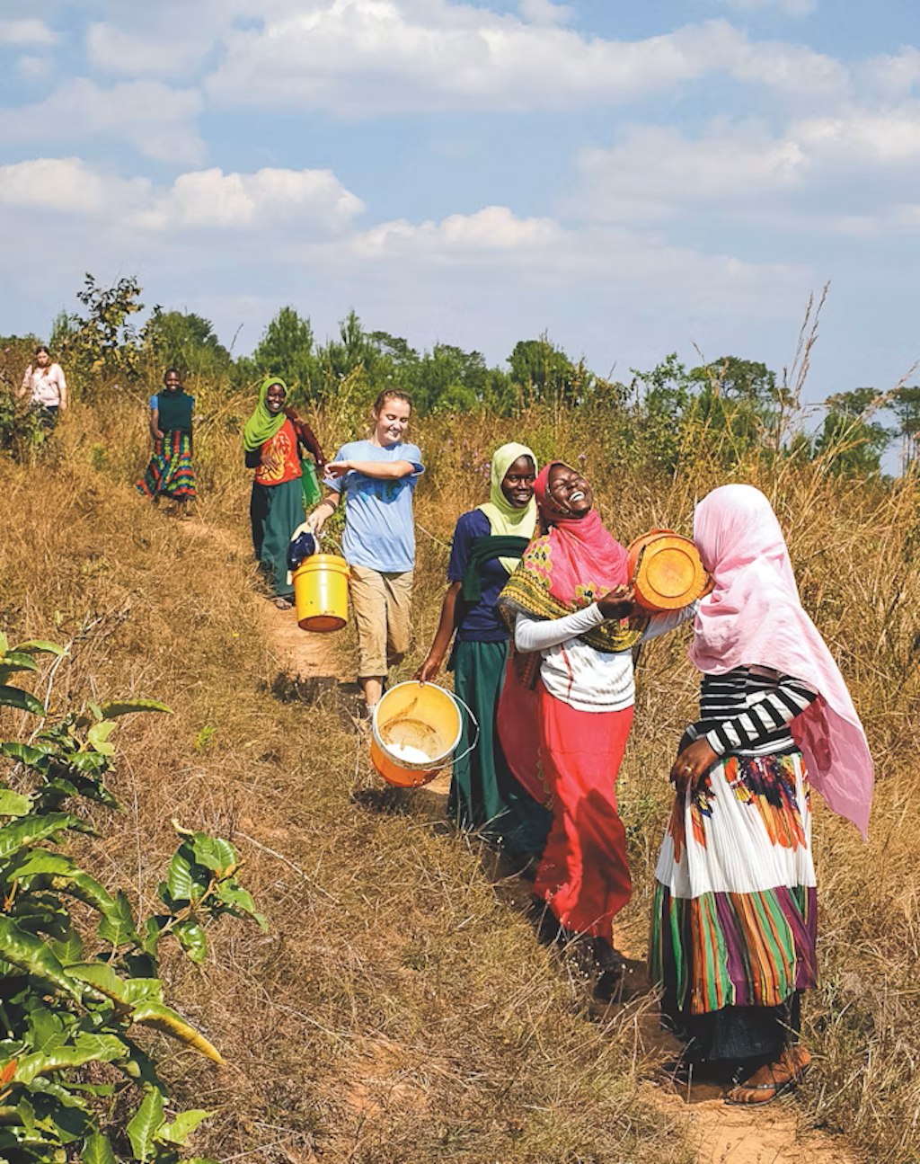 Volunteers and local women carry water together along a rural path in Africa, highlighting teamwork and sustainable water access in public health volunteering abroad.