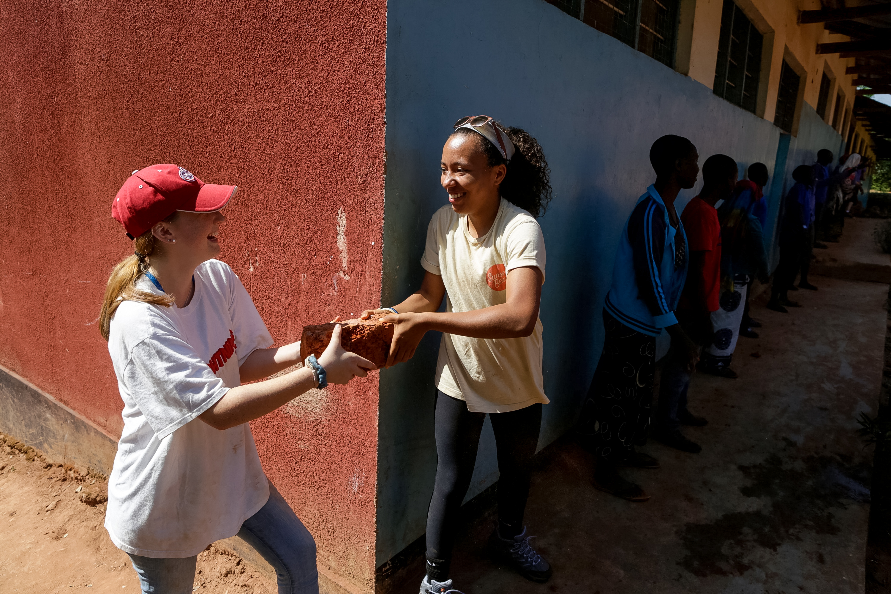 A student and a local student pass a brick during a construction project