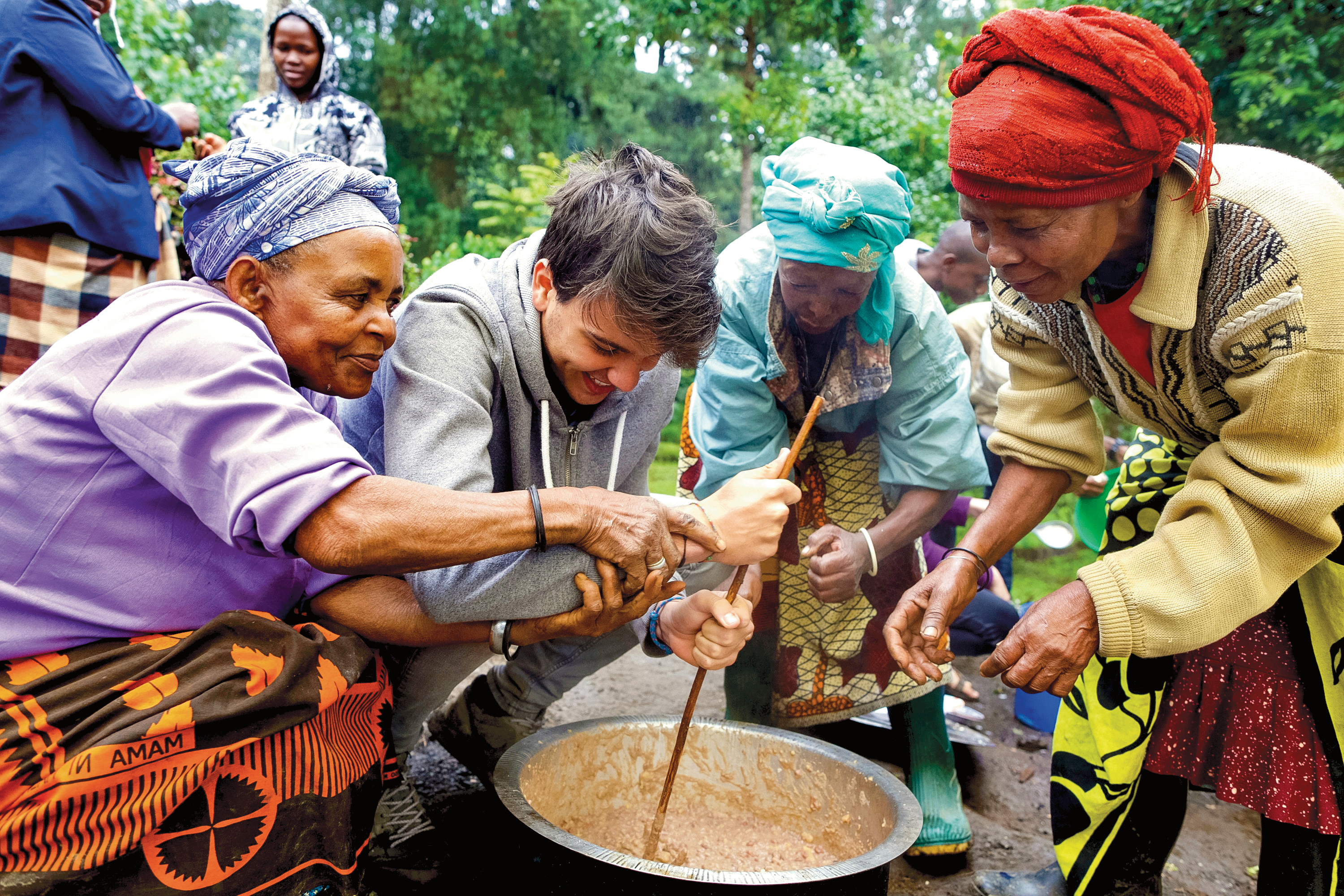 A student stirs a large pot with local women during a community cooking activity in Tanzania