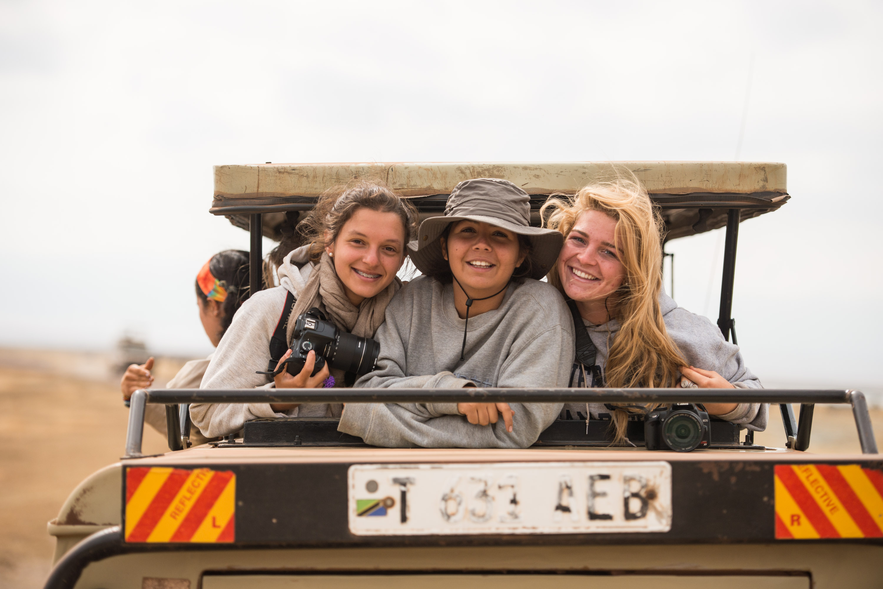 Students in Tanzania smile together in the back of a safari vehicle with cameras in hand