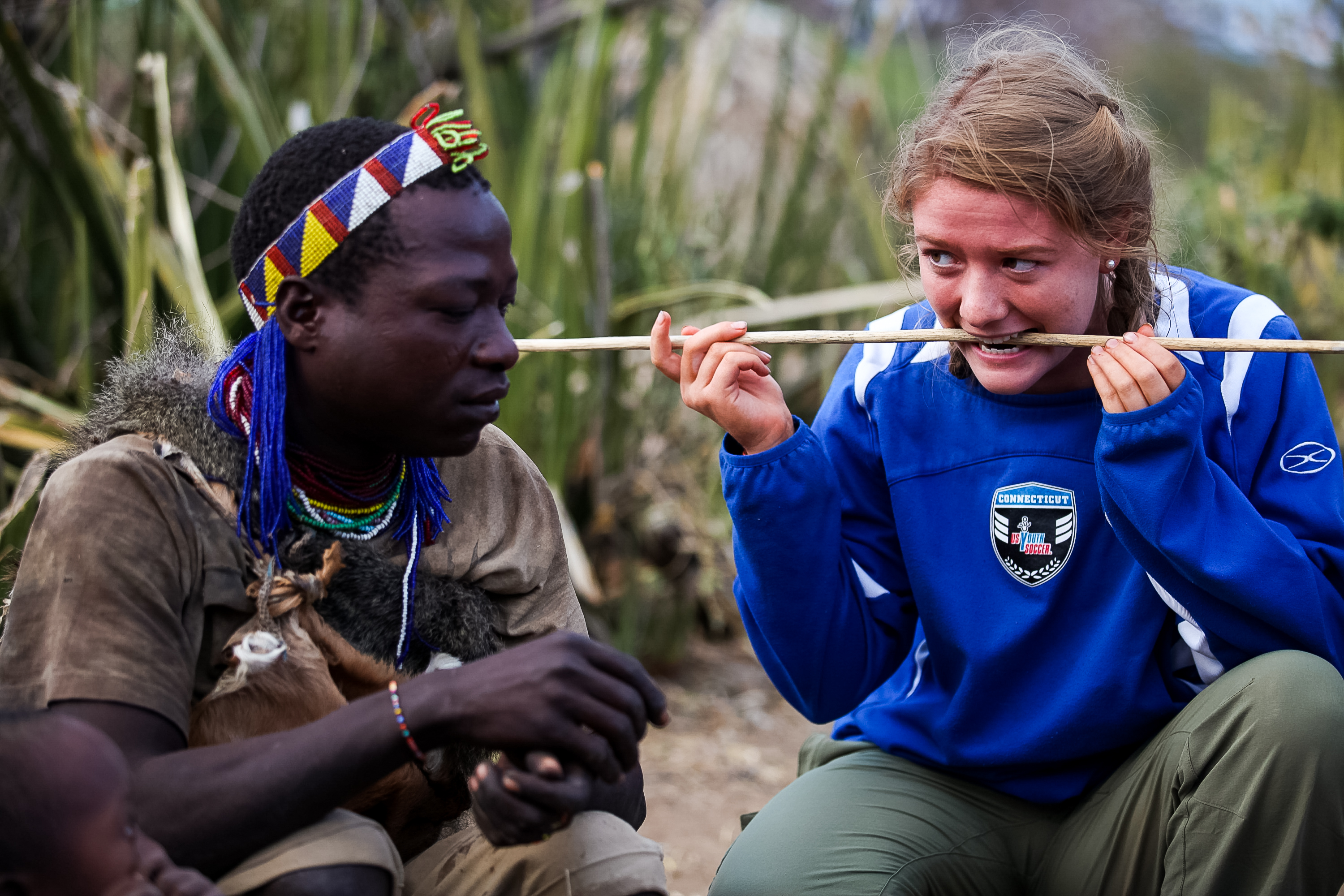 A student bites down on a stick alongside a Hadzabe guide during a bushcraft demonstration