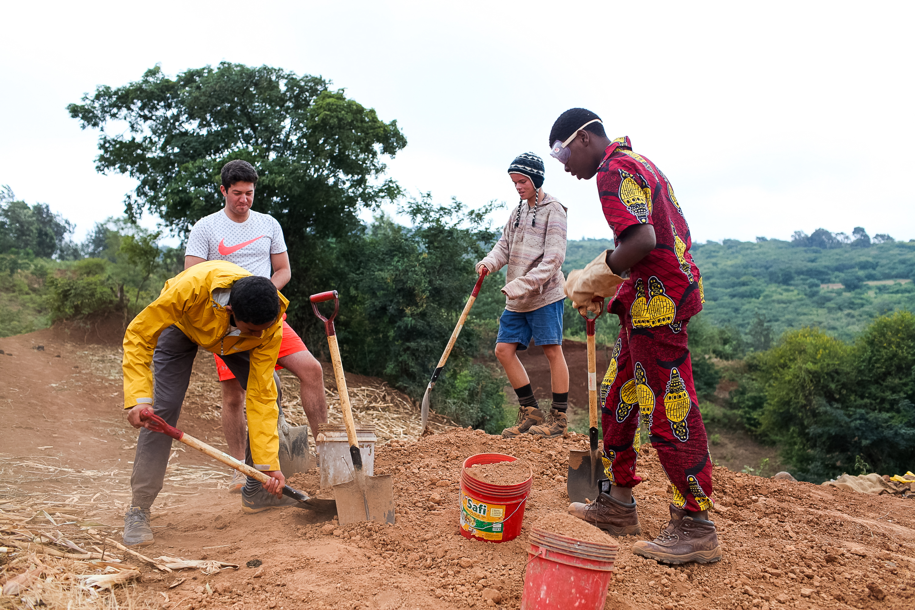 Students dig with shovels alongside a community member on a hillside in Tanzania