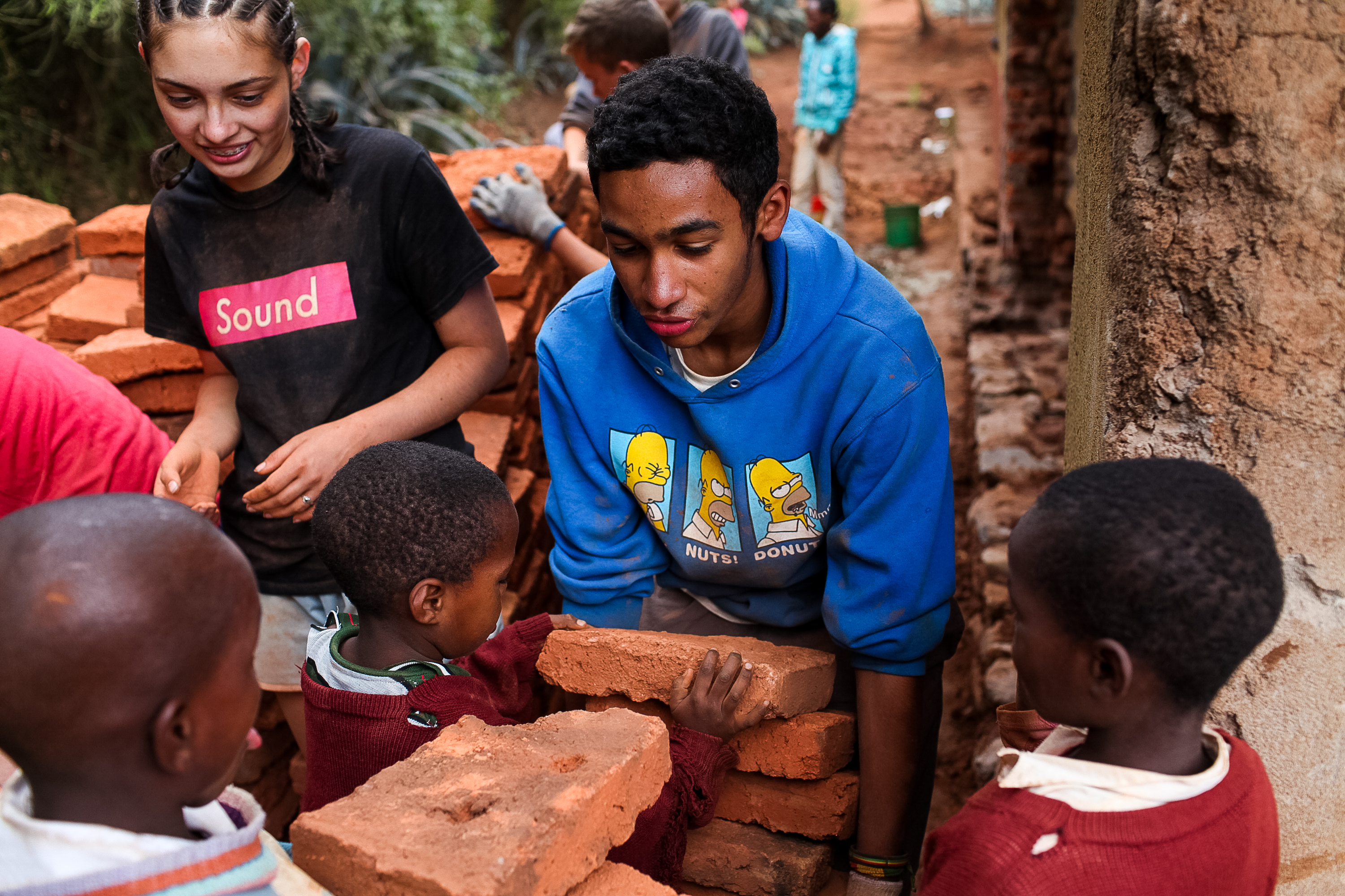 Students stack bricks with local children at a village construction site