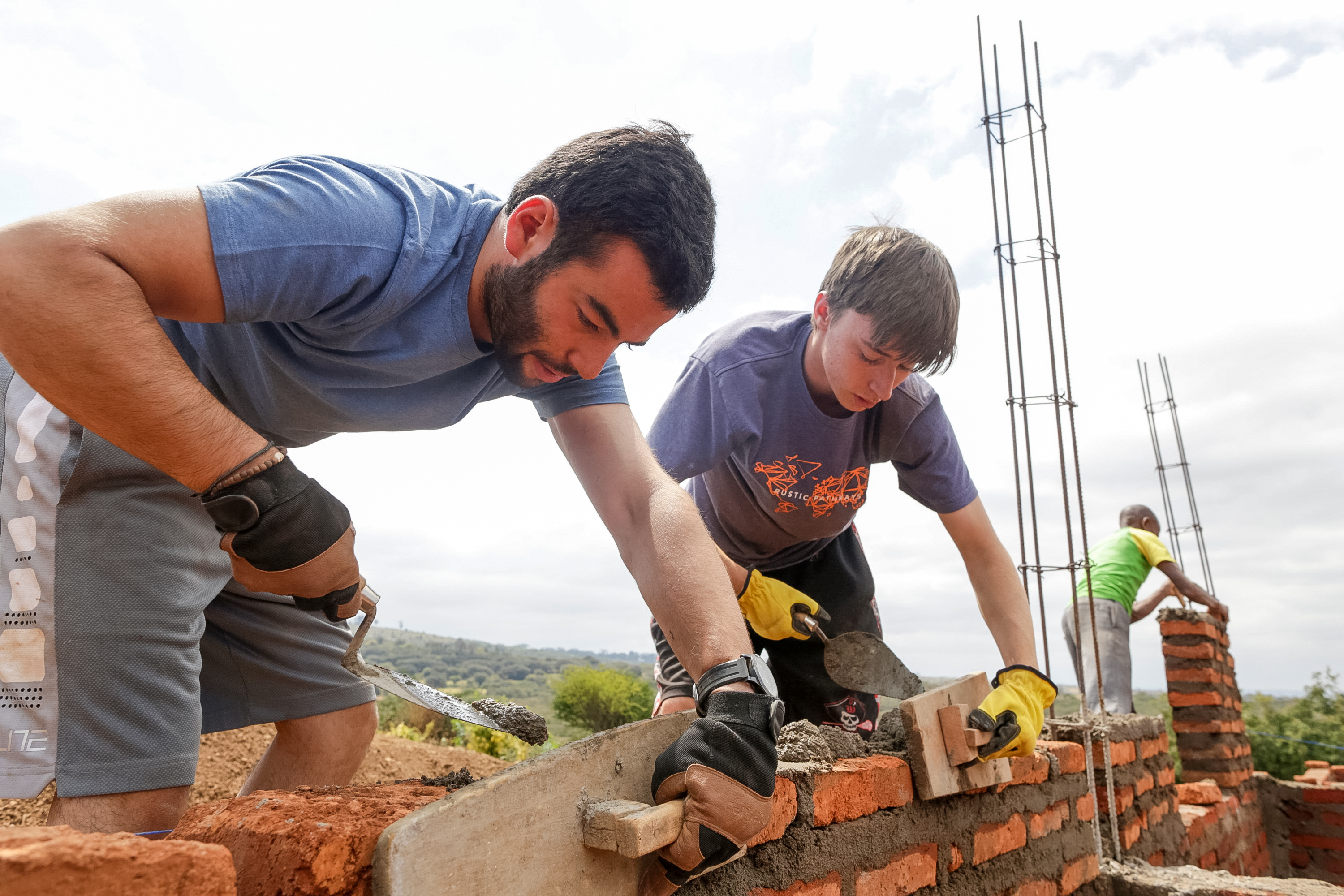 Students lay bricks together on a wall at a construction site
