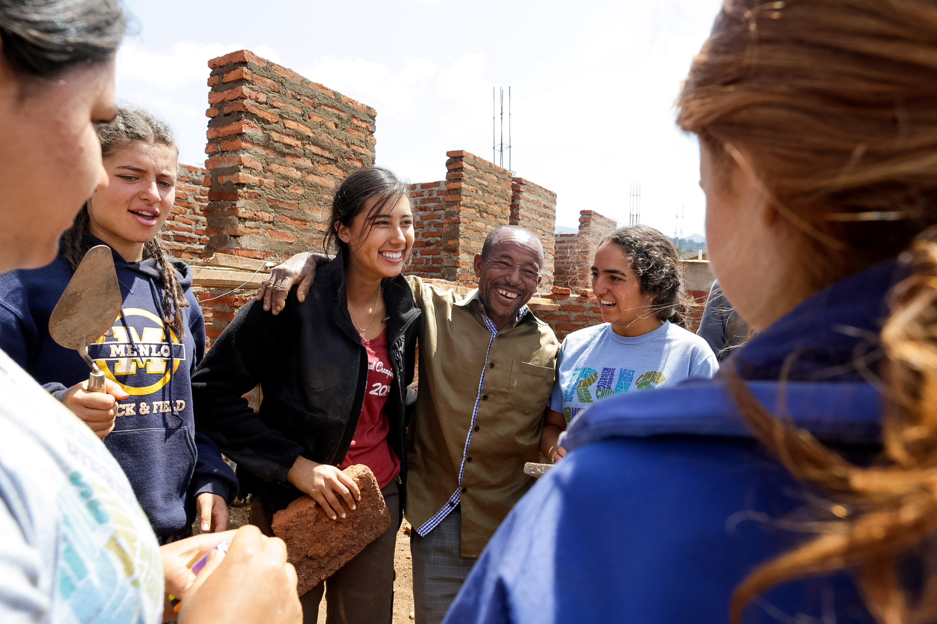 Students share a laugh with a local worker at a brick-making construction site