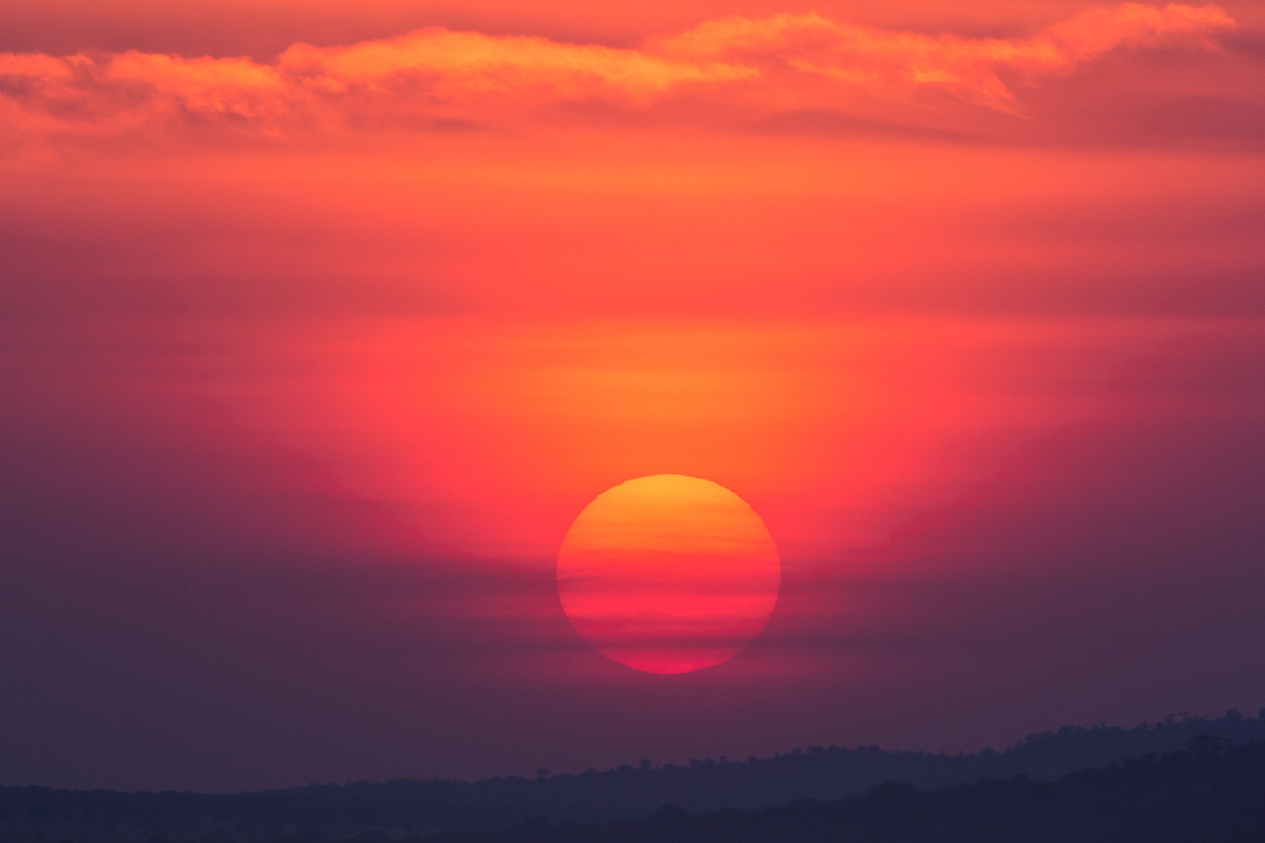 The sun sets in a deep red sky over distant hills