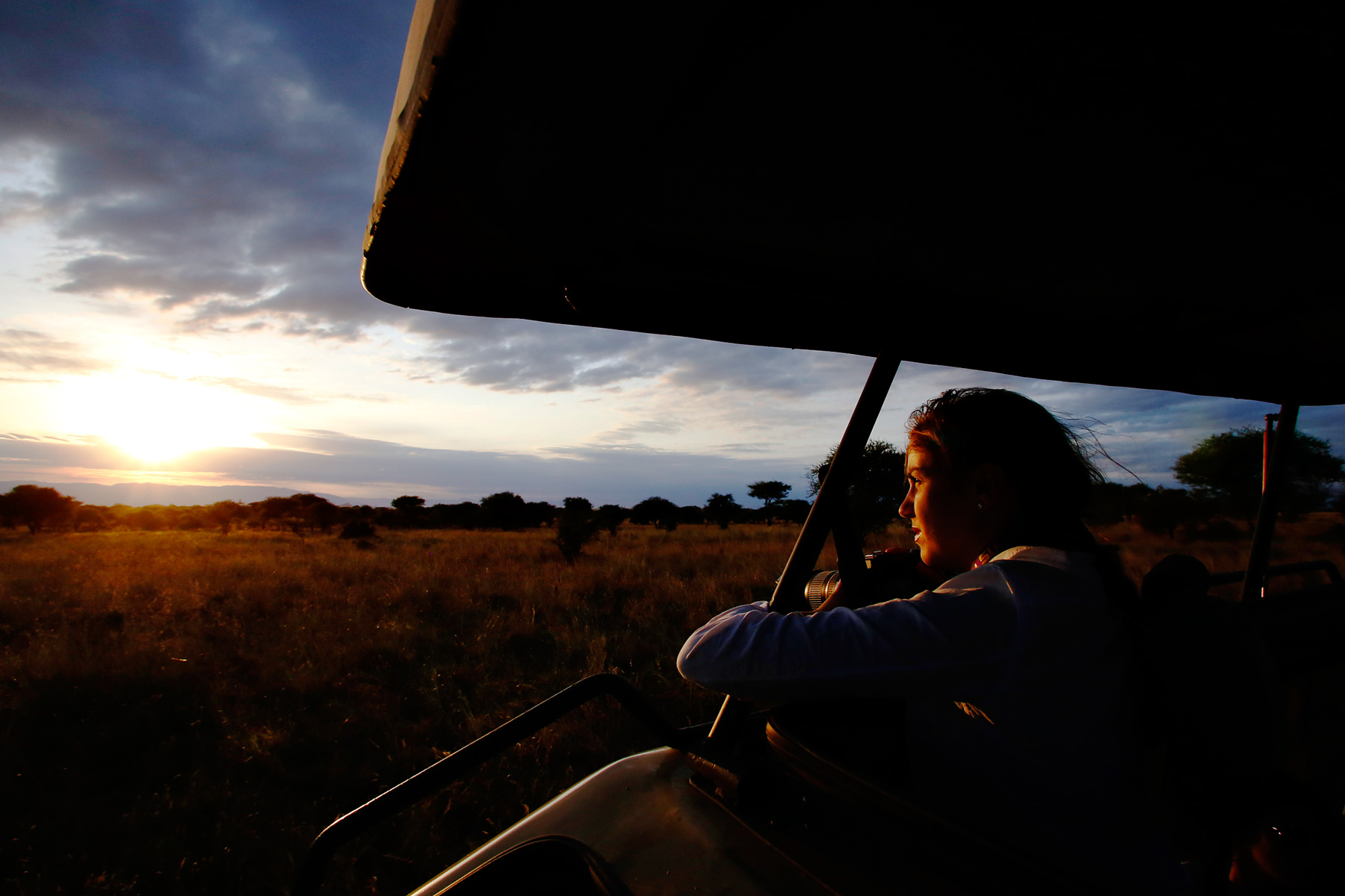 A student watches the sunset over the savanna from a safari vehicle