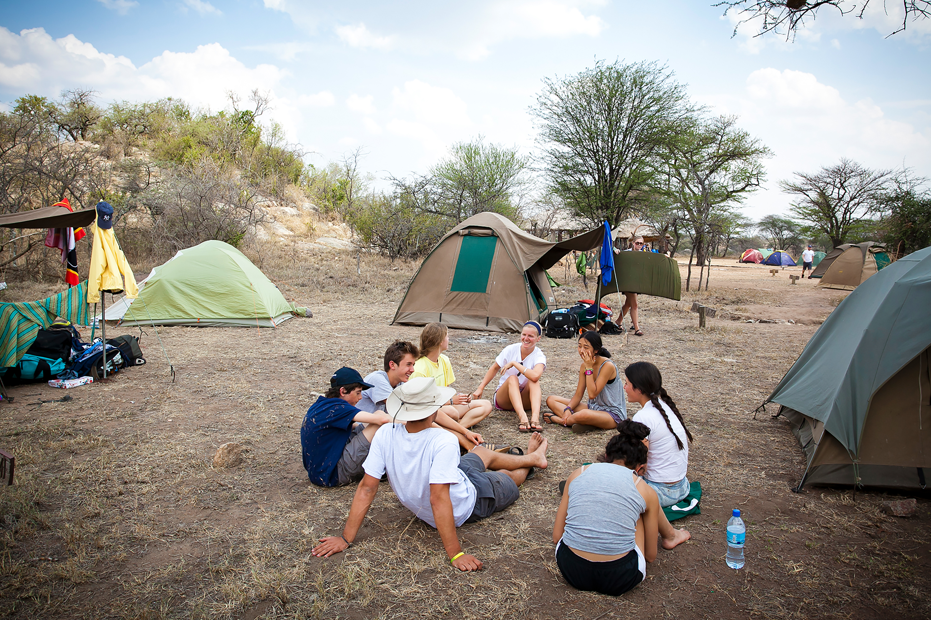 Group of friends sitting and talking at a campsite with tents in the background.