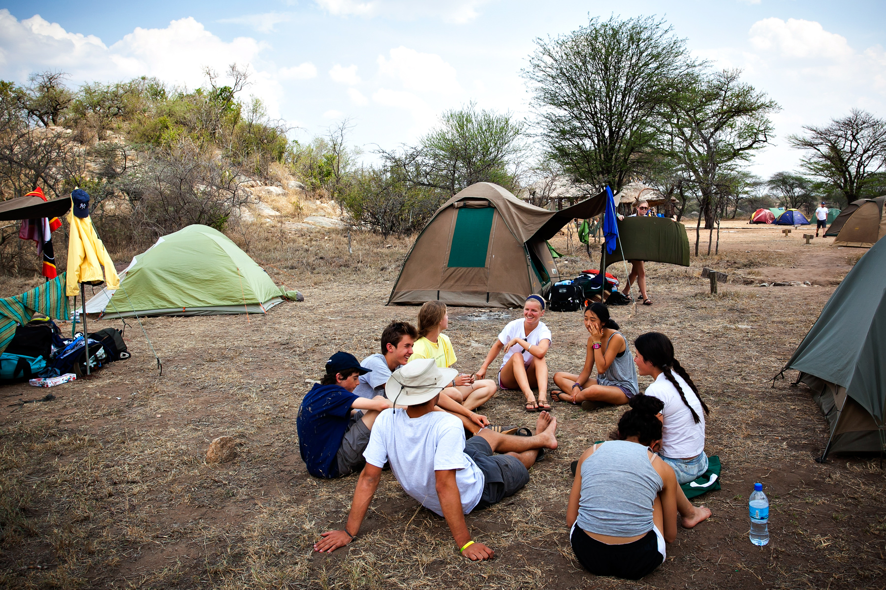 Student travelers sit in a circle chatting at a campsite surrounded by tents