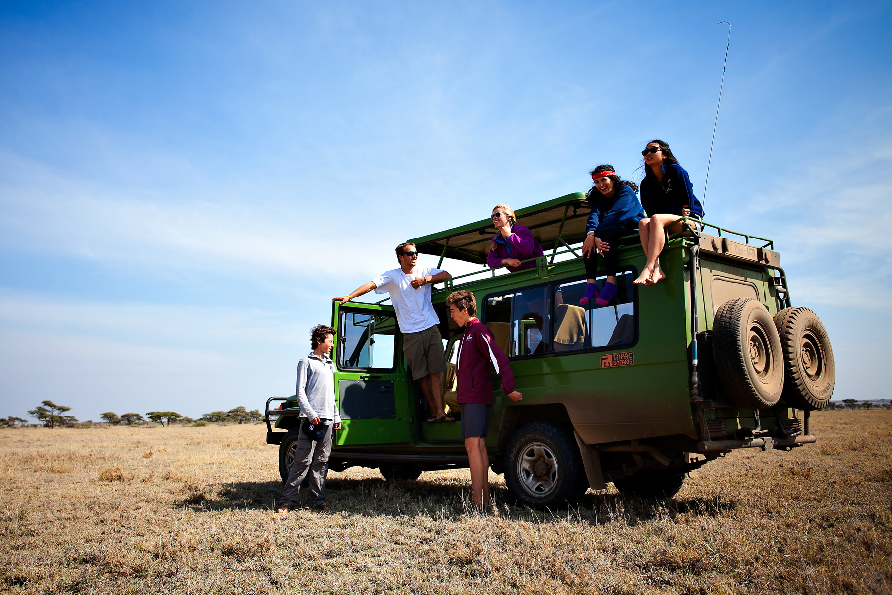 Students gather on and around a safari vehicle on the open savanna in Tanzania