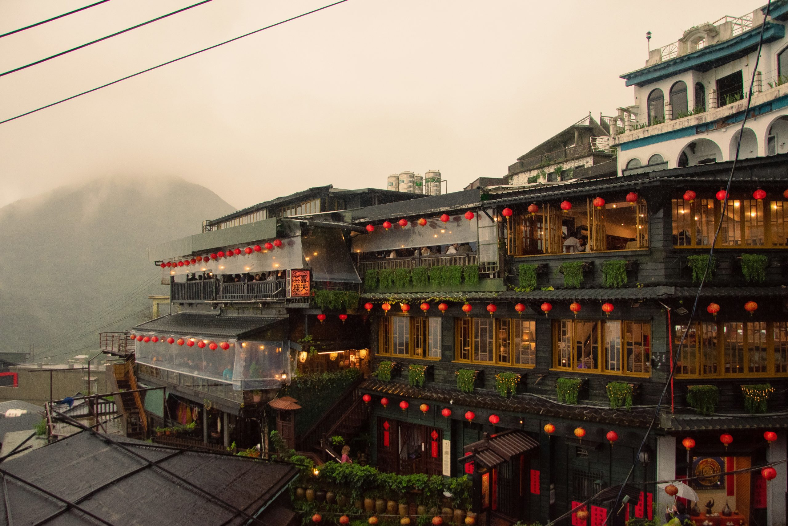 Teahouses strung with red lanterns climbing a hillside in Jiufen, with a misty mountain behind.