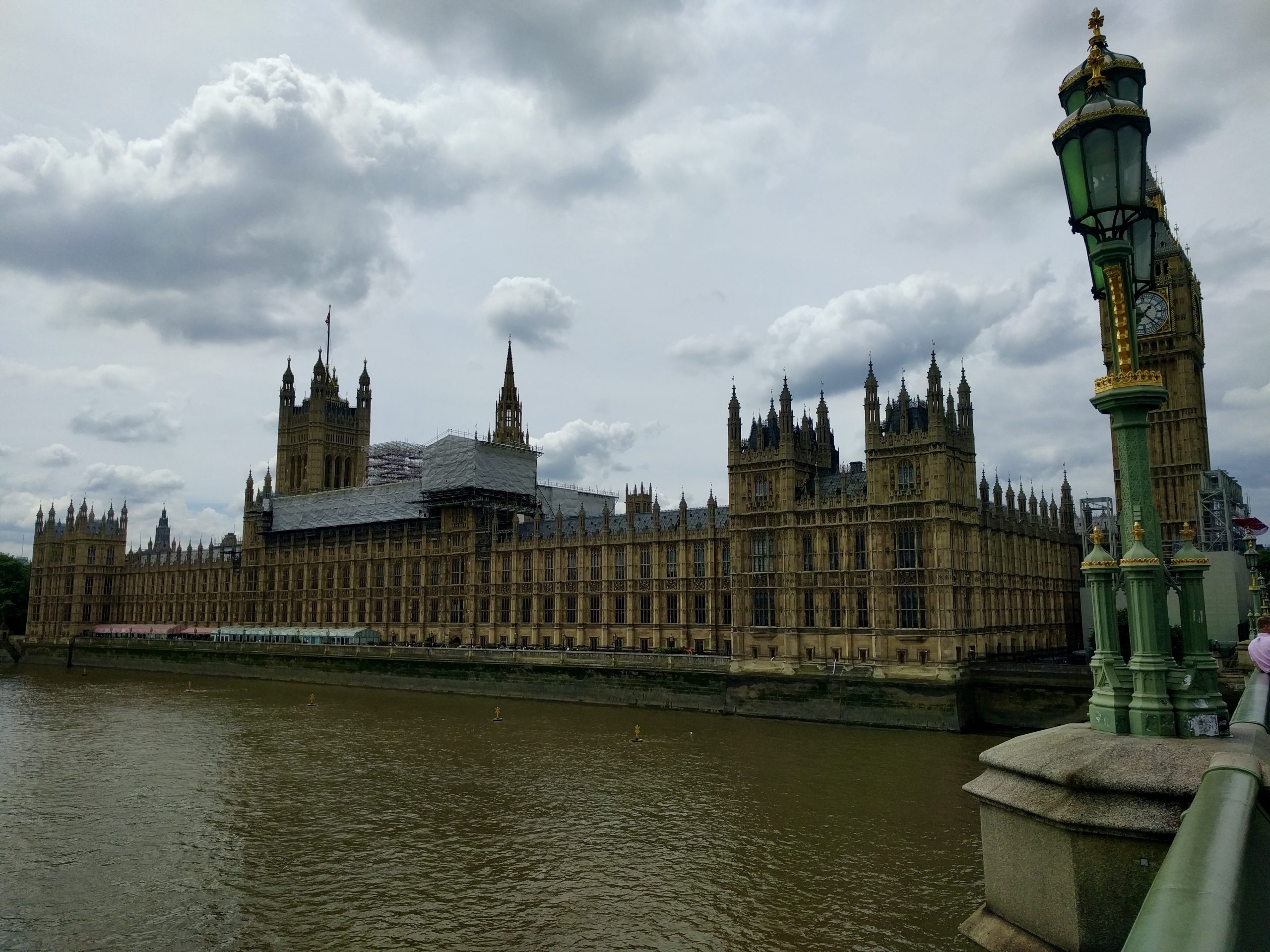 Teen travelers in England view the Houses of Parliament across the Thames under a cloudy sky
