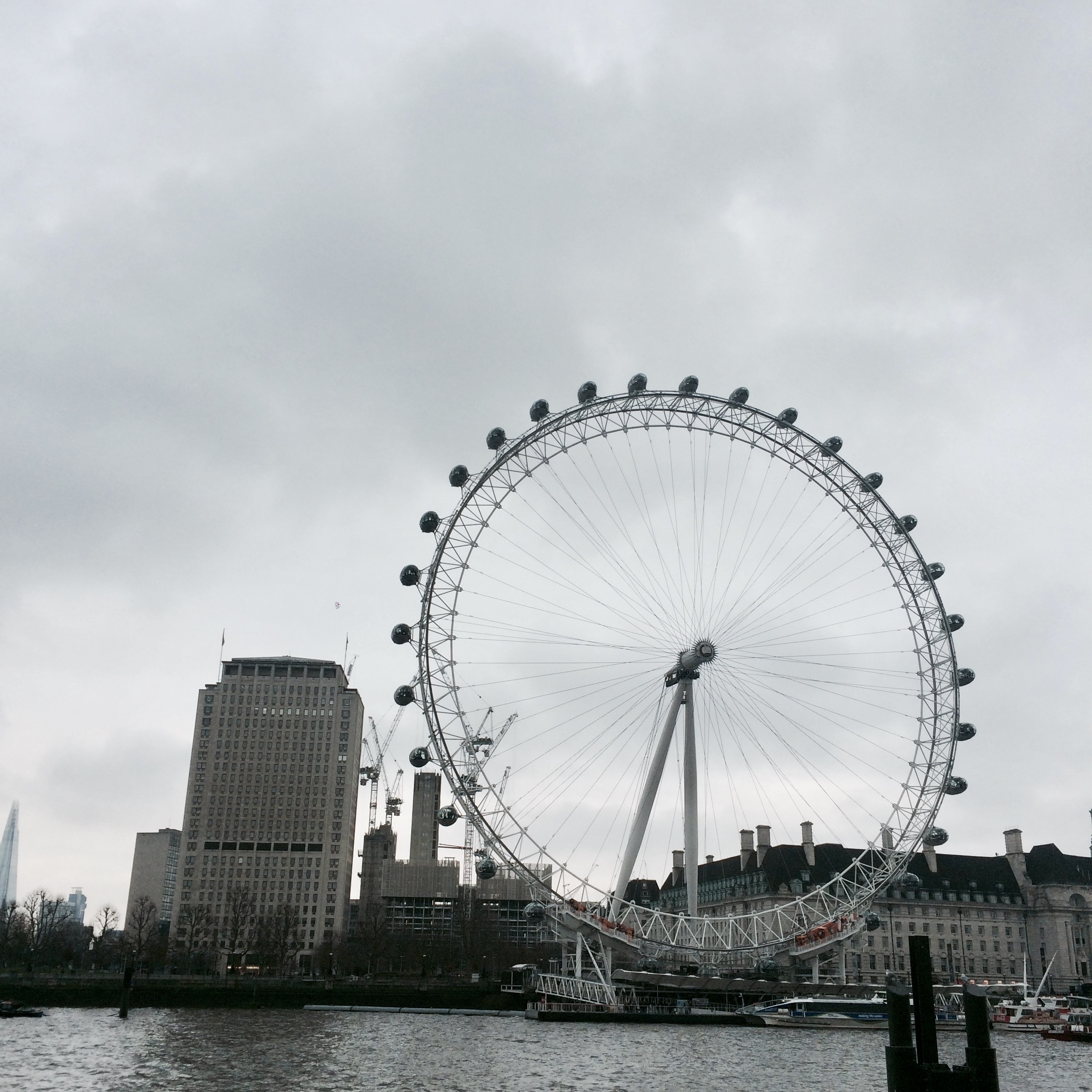The London Eye rises over the Thames skyline in England under an overcast sky