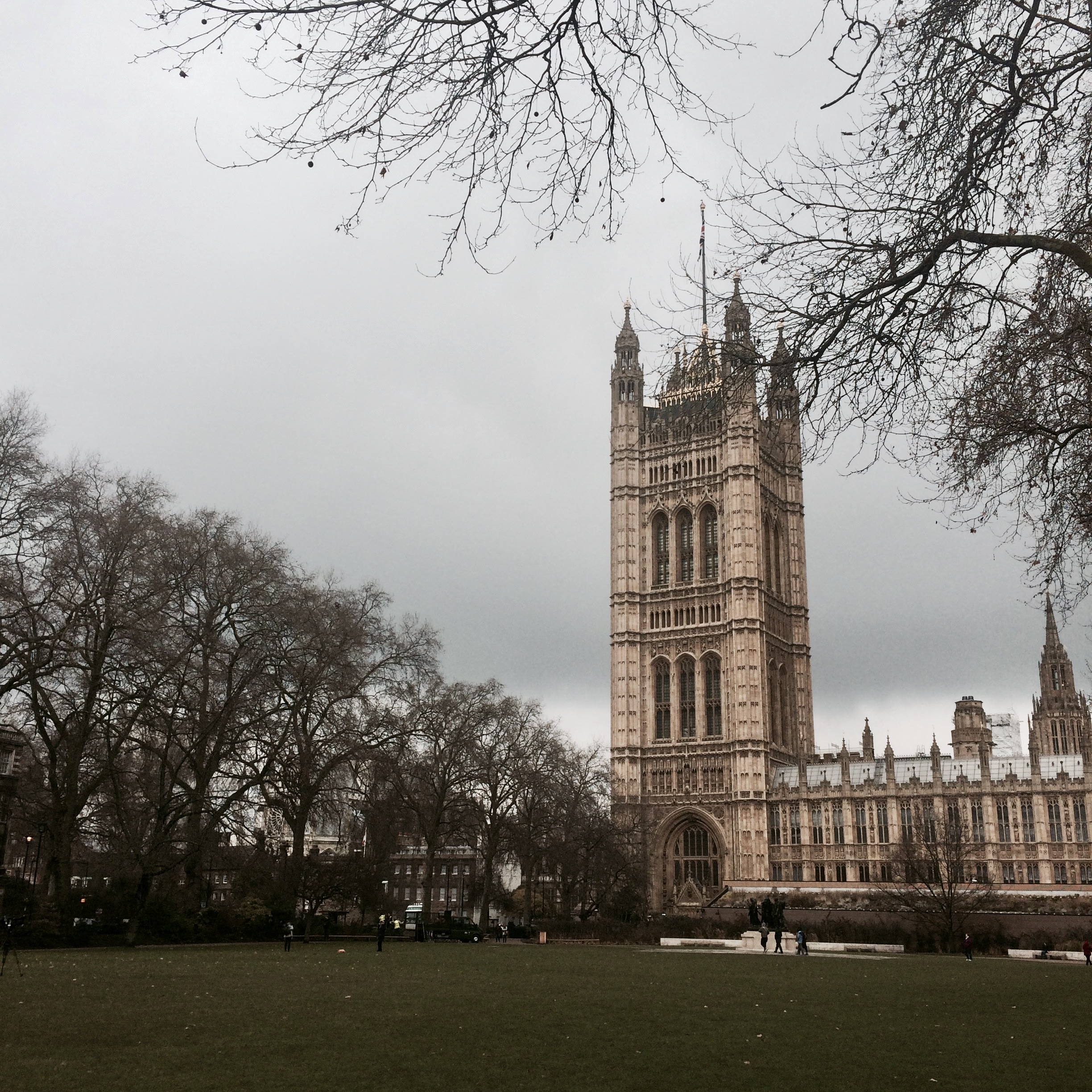 Victoria Tower of the Houses of Parliament seen across a park lawn under a cloudy sky