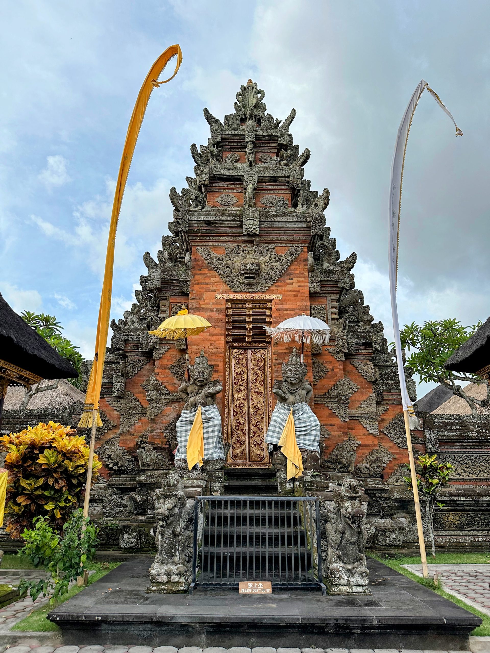 A traditional Balinese temple with intricate carvings and statues draped in yellow cloth, surrounded by lush greenery.