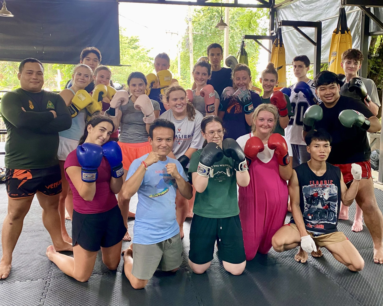 Teen travelers in boxing gloves pose in two rows with Thai trainers under the roof of a Muay Thai gym in northern Thailand.