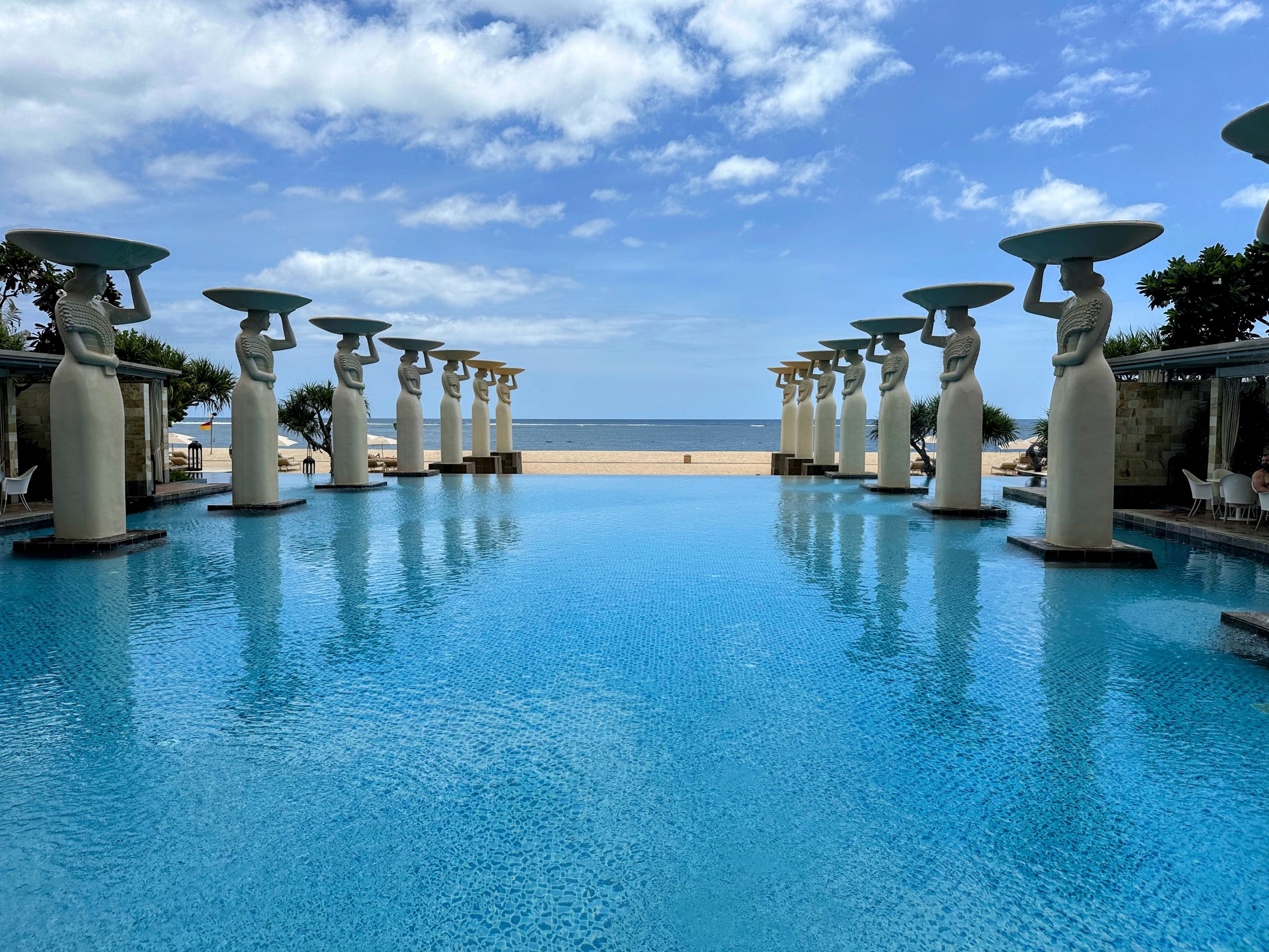 Infinity pool at The Mulia Hotel in Bali with rows of statues overlooking the ocean.