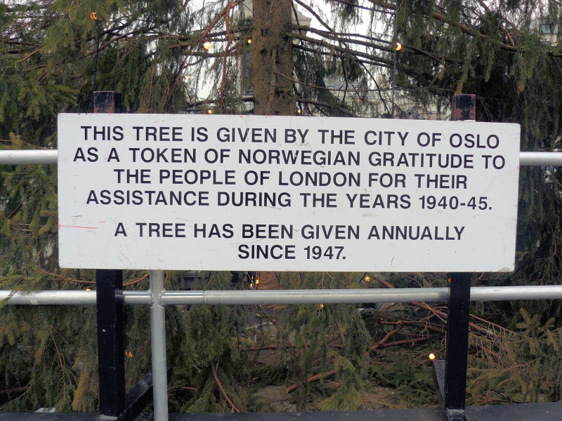 Mike Fleming, CC BY 2.0 <https://creativecommons.org/licenses/by/2.0>, via Wikimedia Commons Sign at the Trafalgar Square Christmas tree explaining the tree is a gift from the city of Oslo in gratitude for British assistance to Norway during WWII.