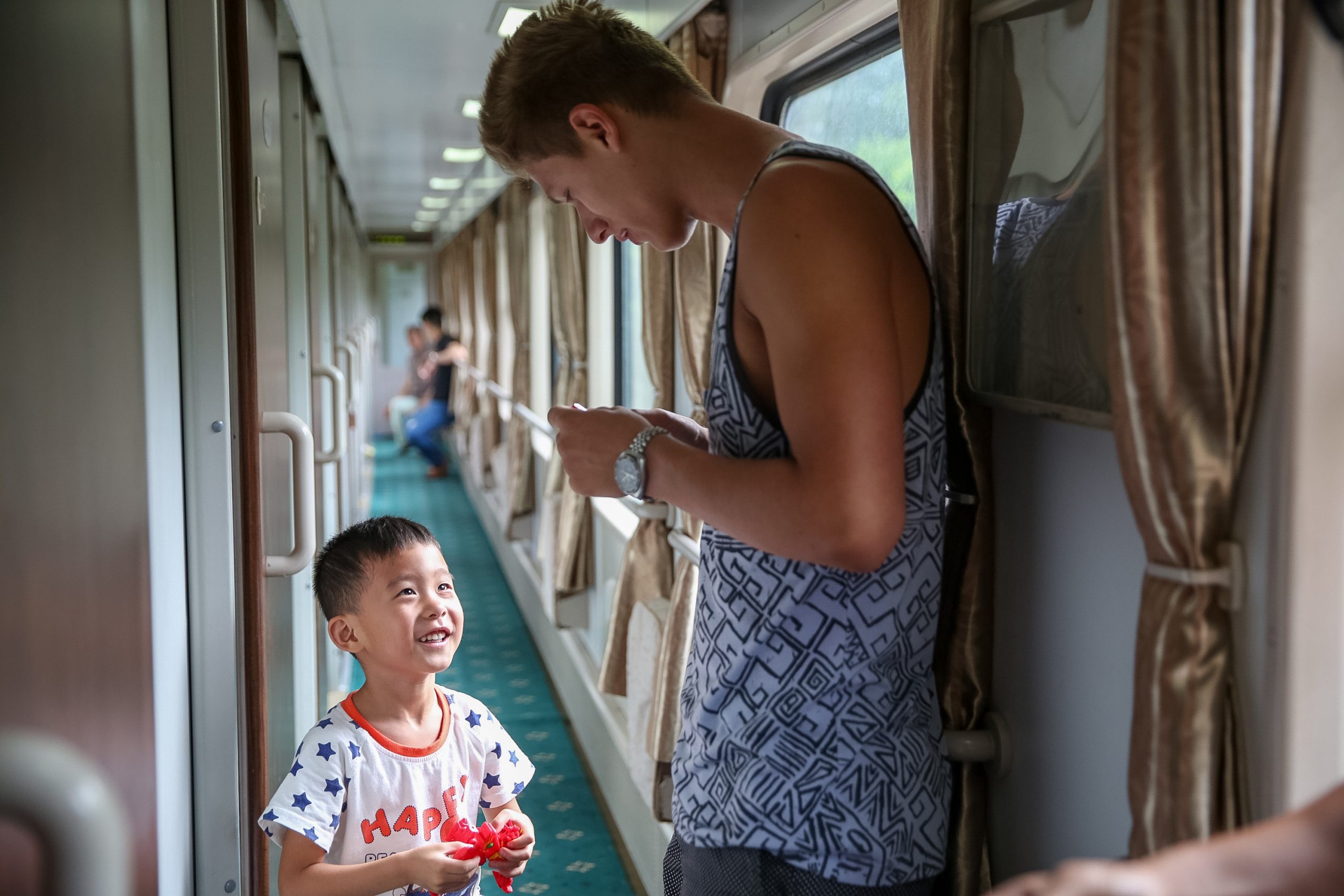 Student travelers laugh with a young boy holding a toy in a train car hallway