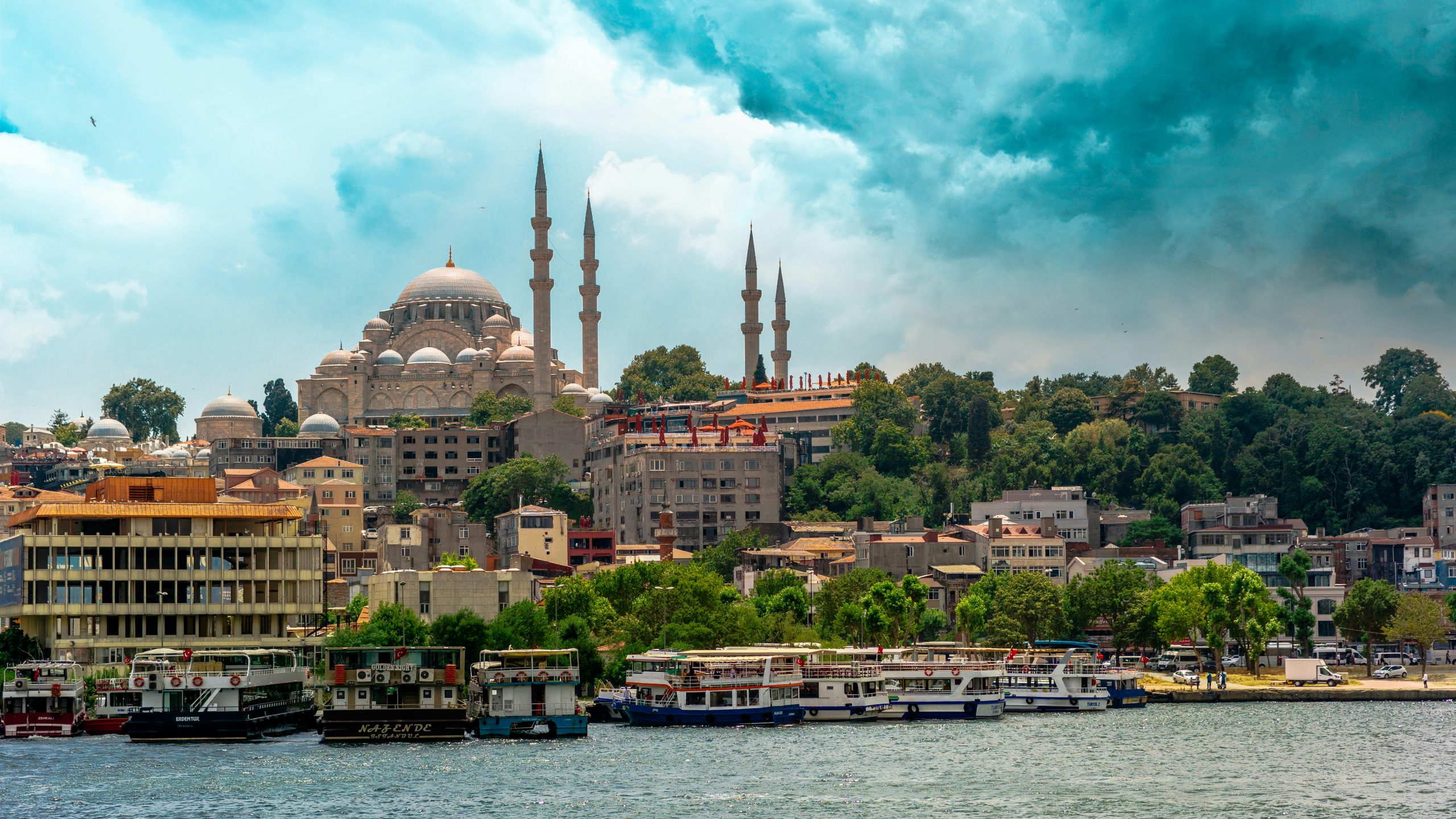 The domes and four minarets of the Süleymaniye Mosque above Istanbul's waterfront, with passenger ferries moored along the shore.
