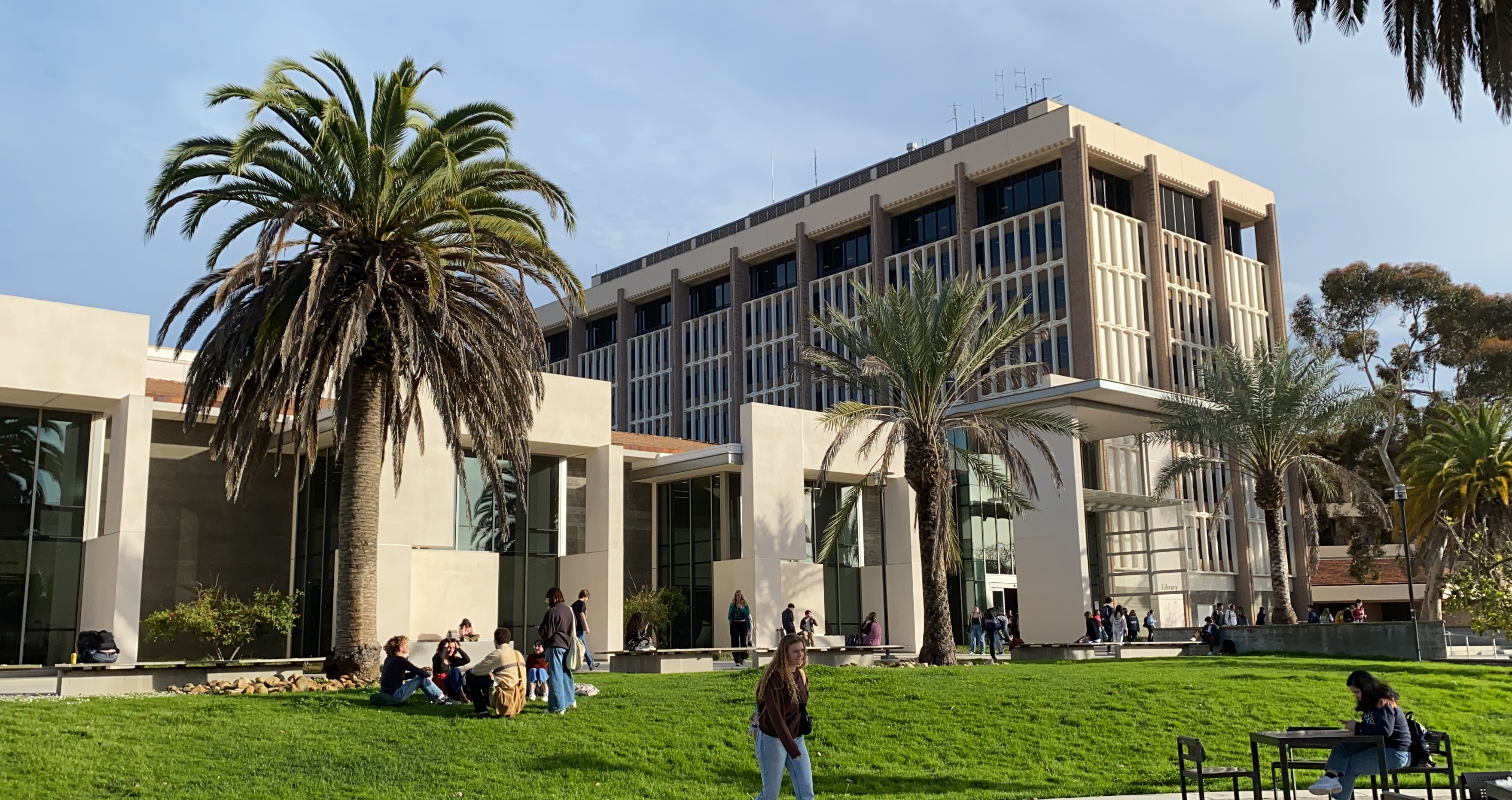 University of California, Santa Barbara campus with students relaxing on the grass, surrounded by palm trees.