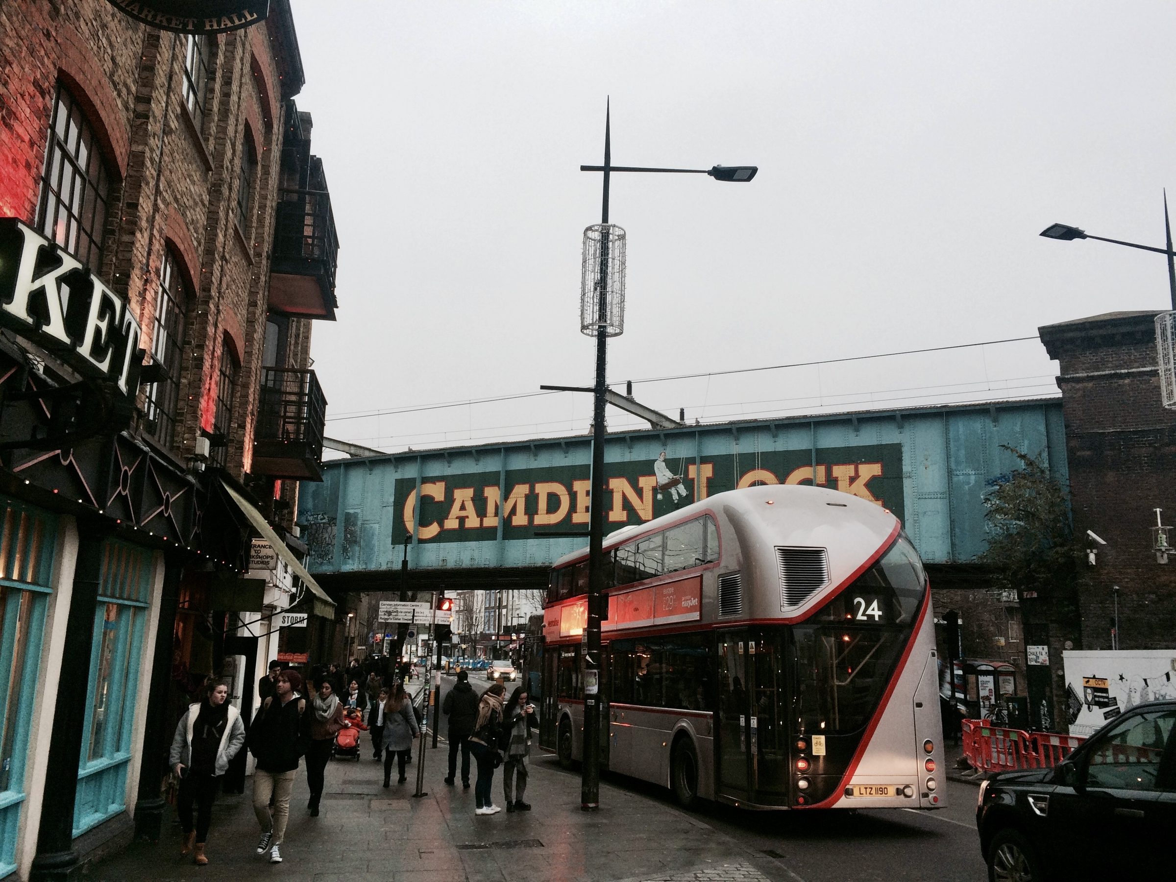 A red double-decker bus passing under the Camden Lock railway bridge