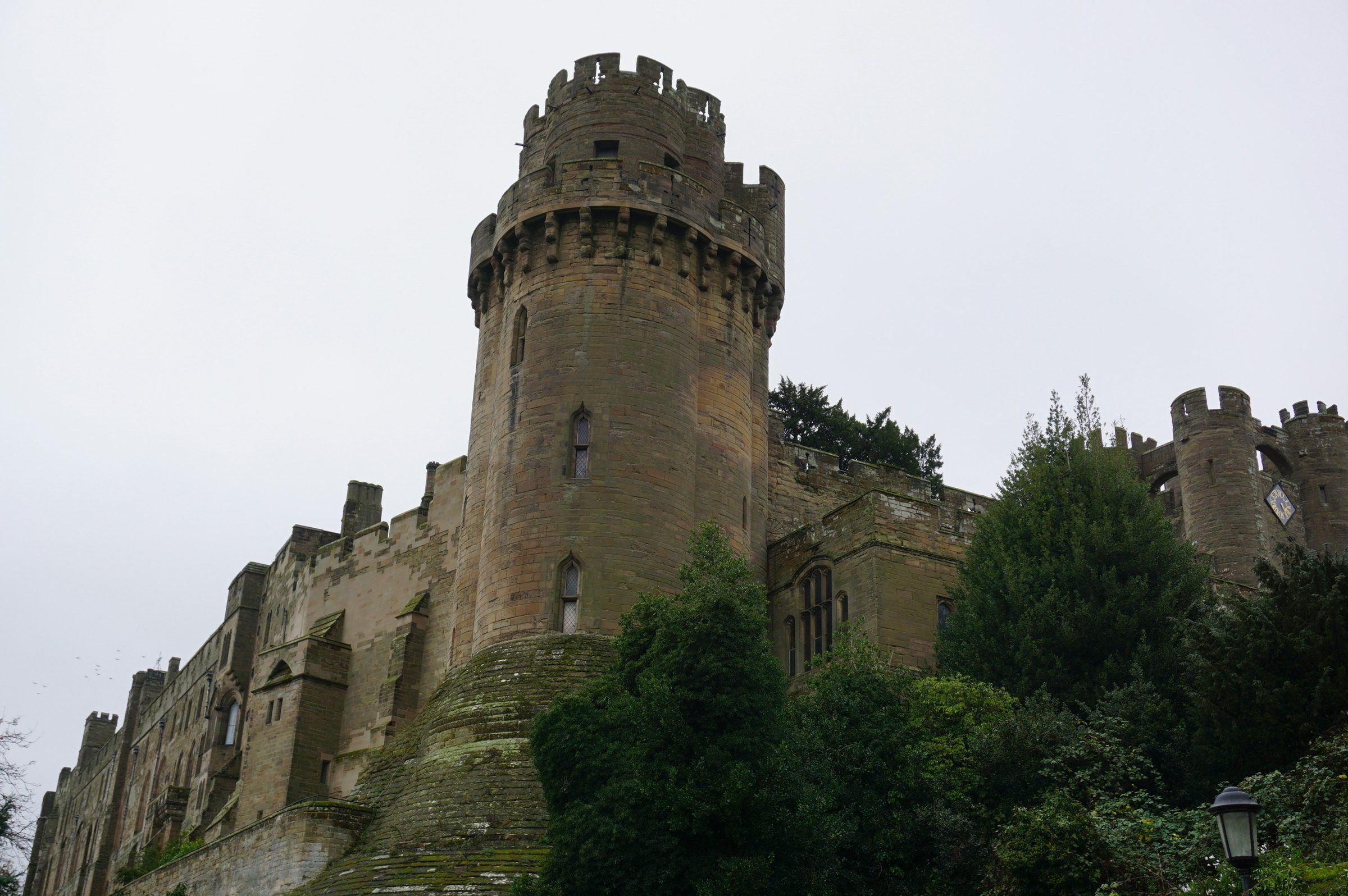 The round tower and battlements of Warwick Castle above the trees