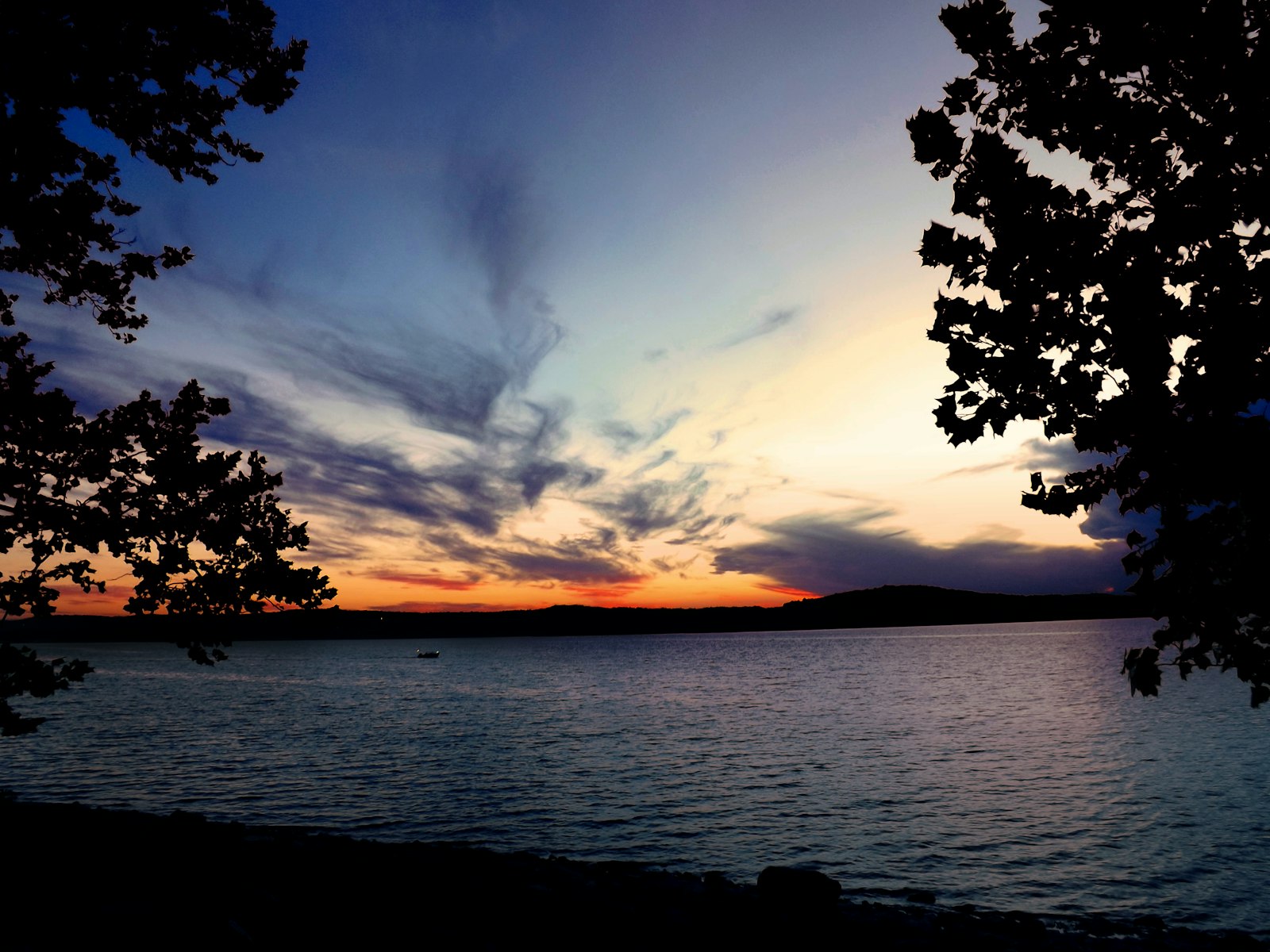 Table Rock Lake at sunset, framed by oaks, with the Ozark ridgeline on the horizon.